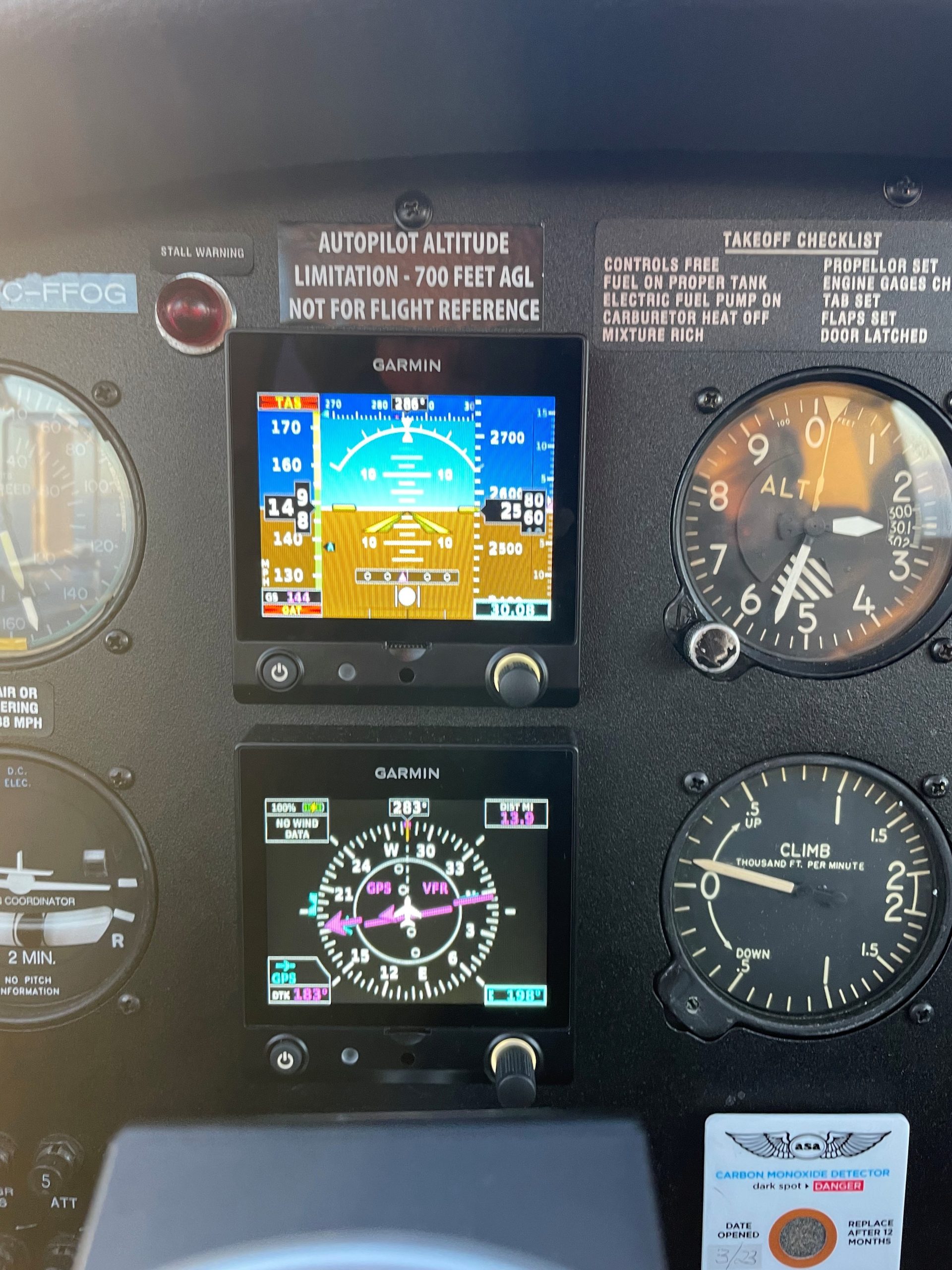 Cockpit panel with Garmin flight displays and attitude indicator among analog gauges and warning labels, in a small aircraft cockpit.
