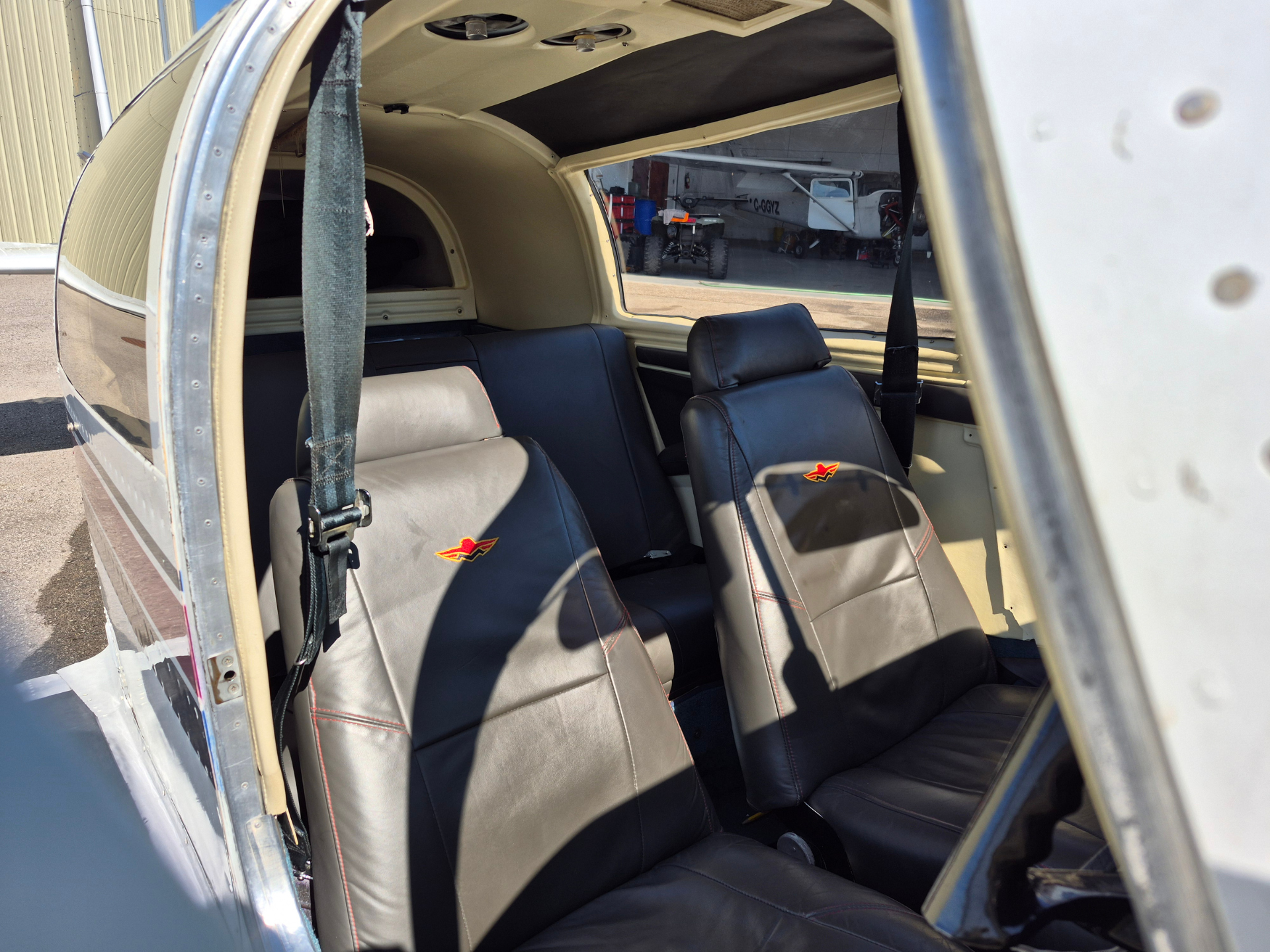Interior of a small airplane with black leather seats and red stitching, opened door showing outside hangar and another aircraft nearby