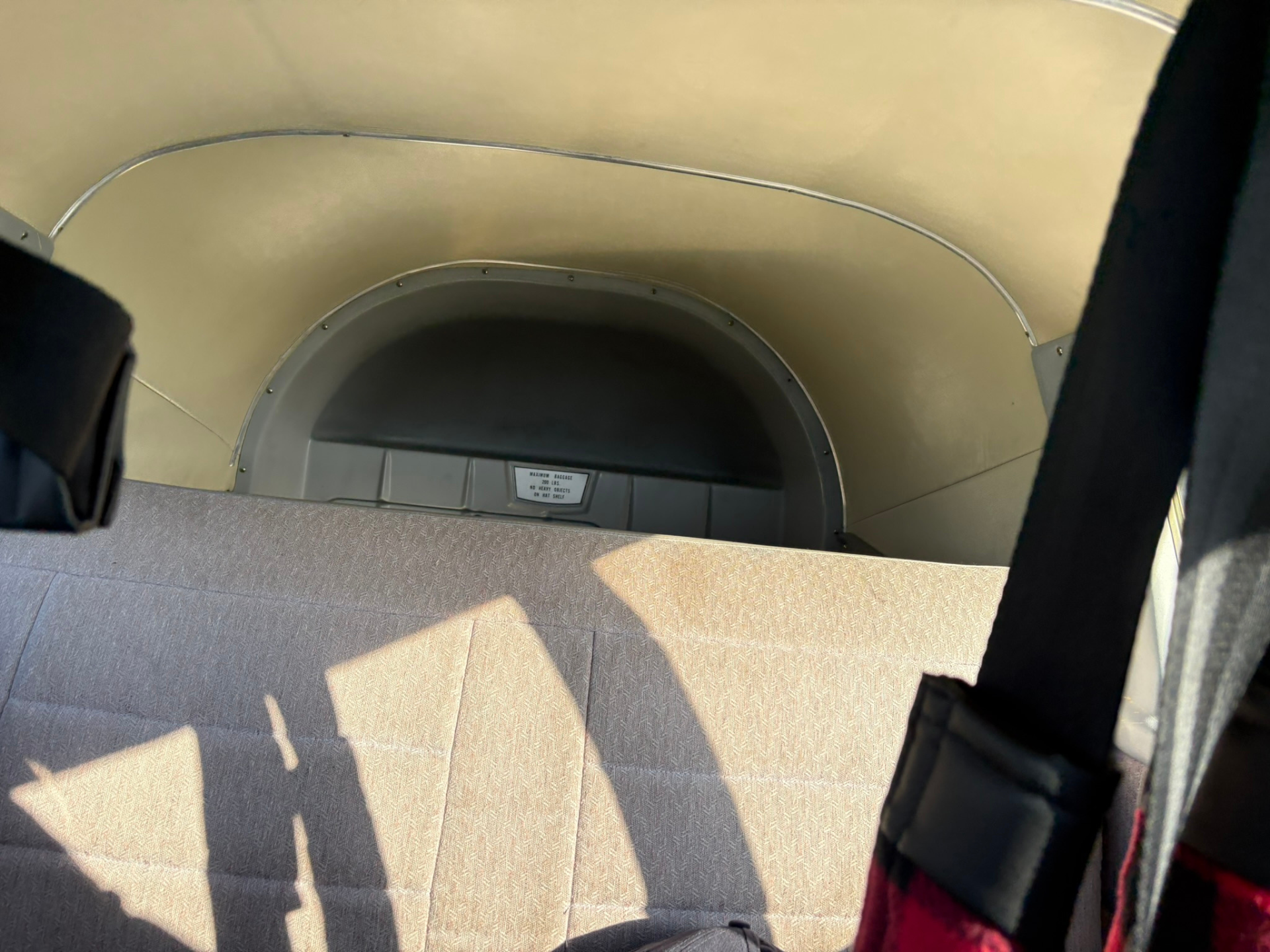Interior of a vehicle/storage area showing a circular opening or hatch with a beige curved wall and seat belts in the foreground.