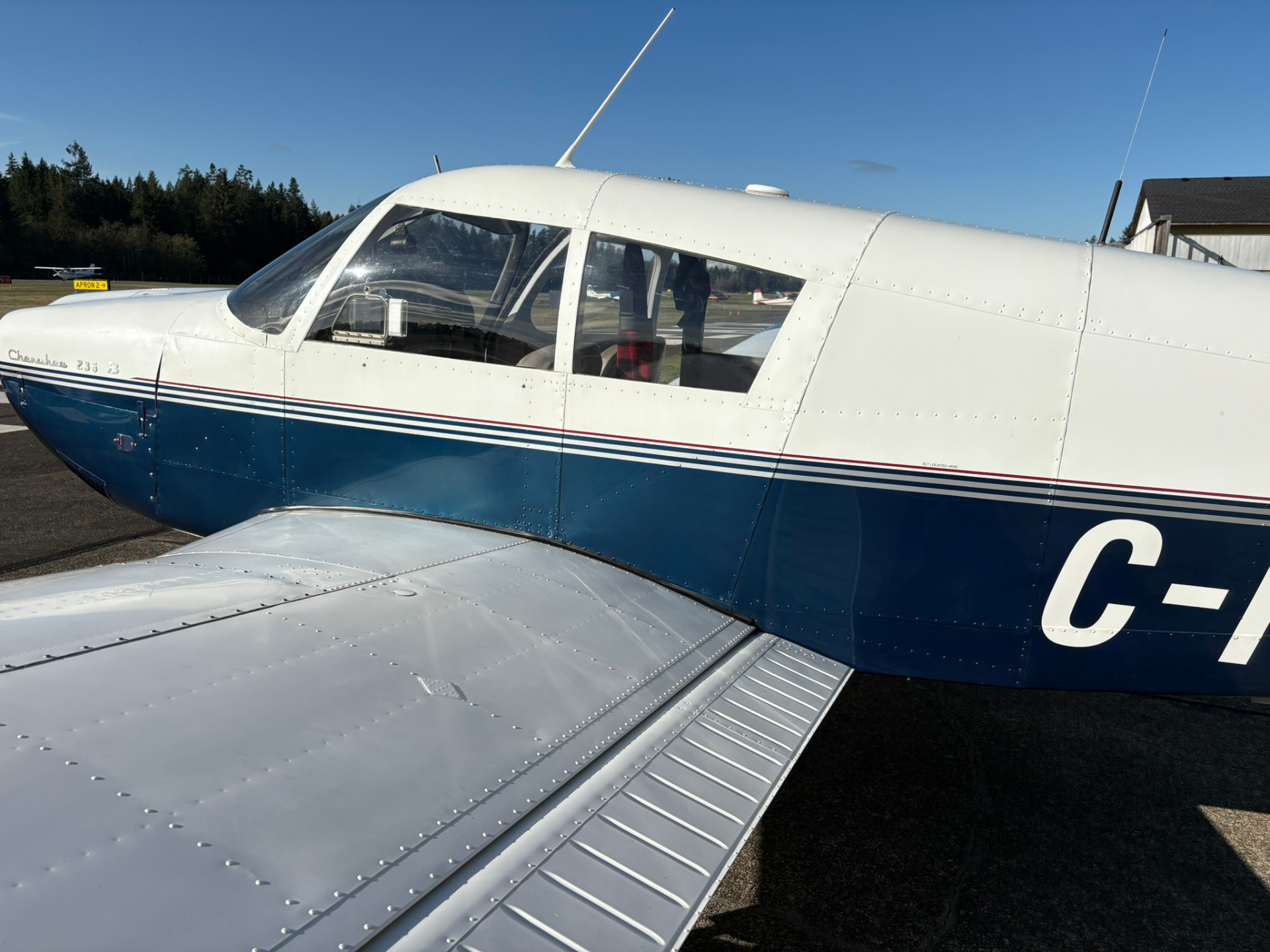 Close-up view of a small silver-and-blue airplane on a tarmac, cockpit windows visible and riveted wing in the foreground.