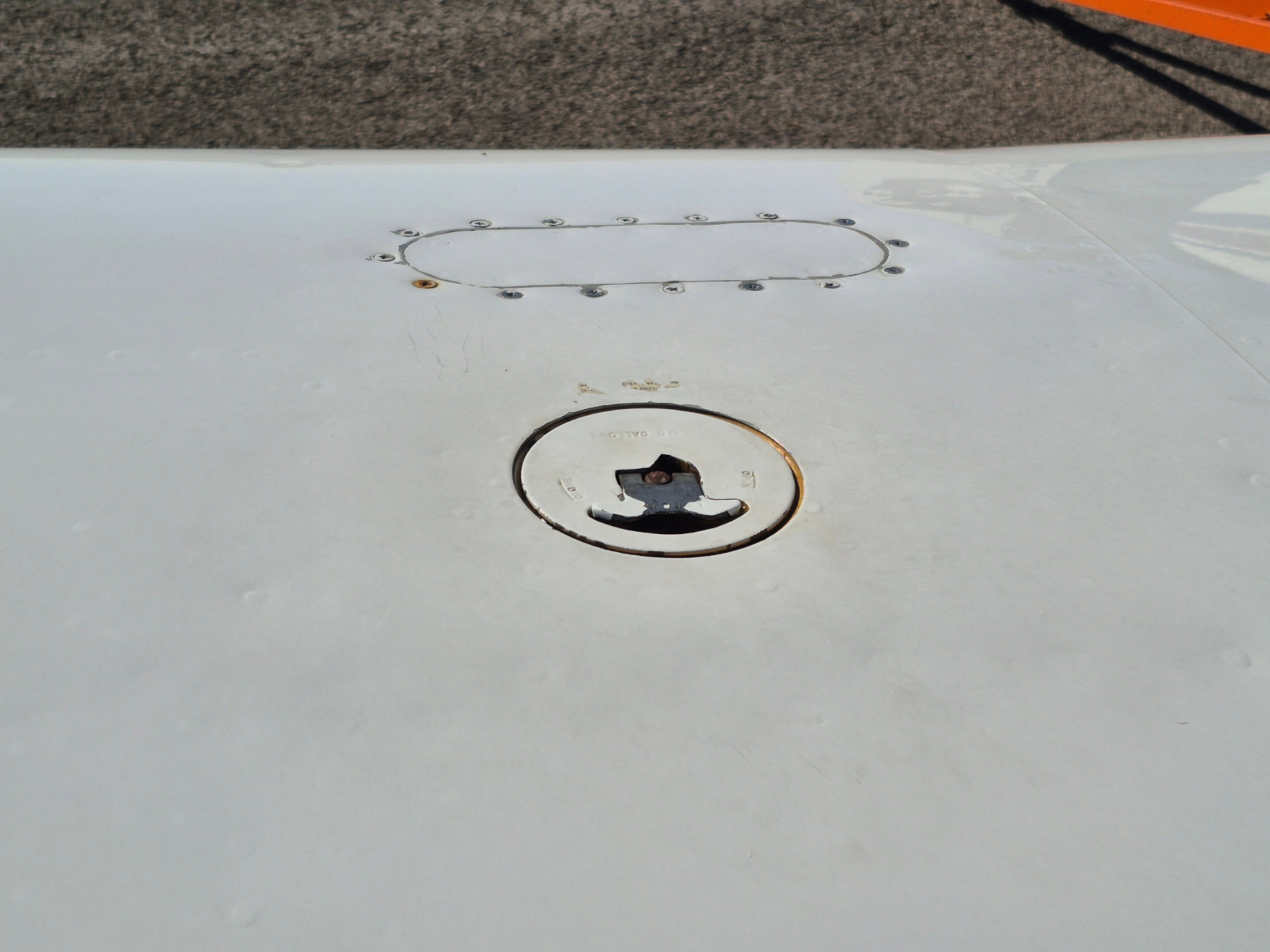 Top of an airplane wing with a circular access hatch and surrounding screws.