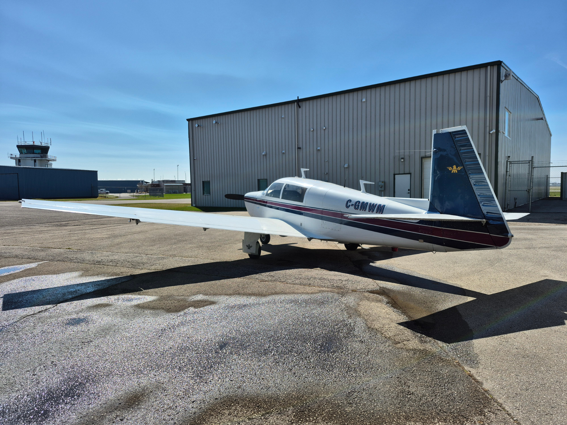Small single-engine airplane parked on the tarmac beside a large metal hangar under a clear blue sky.