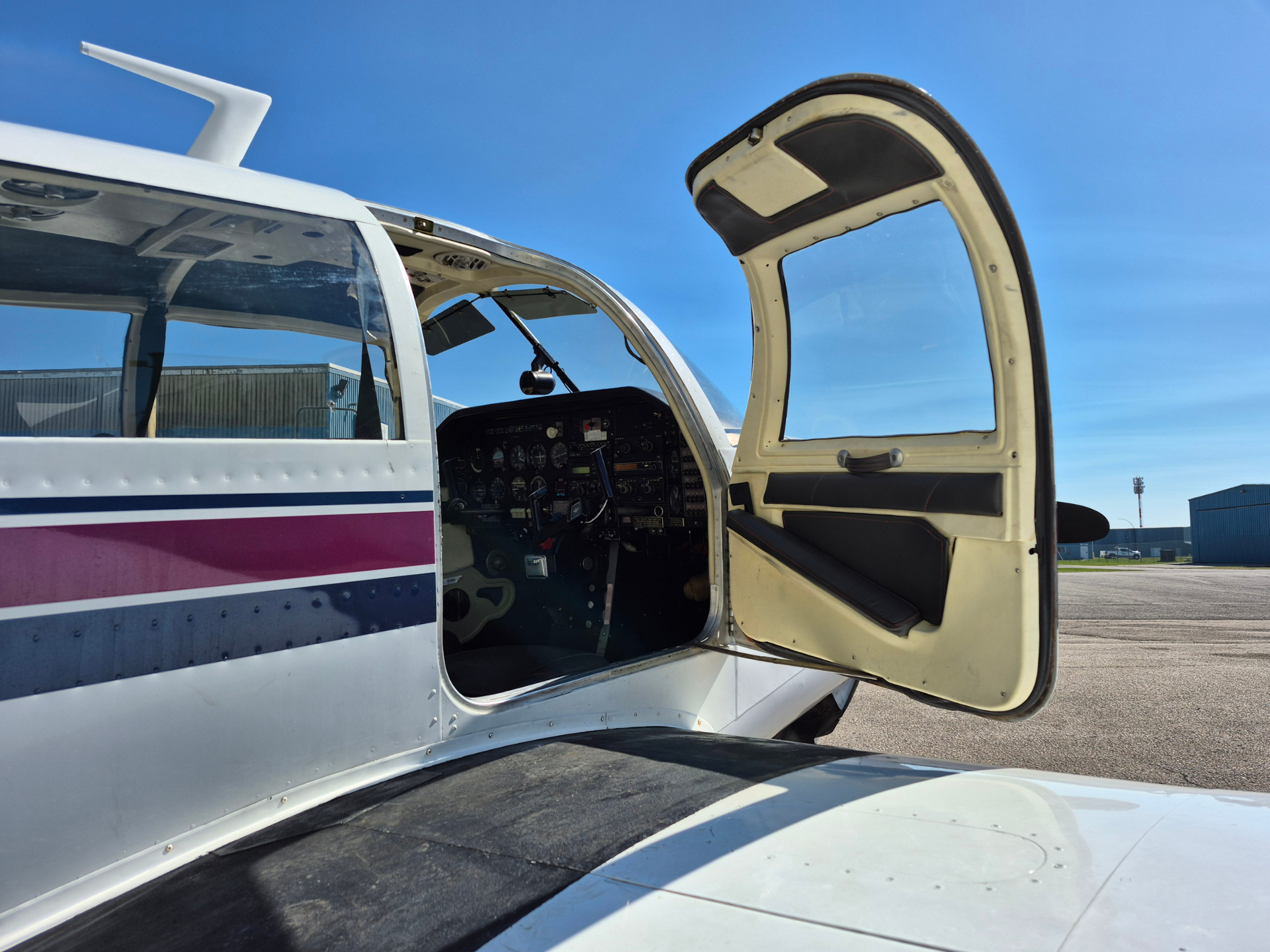 Small white private airplane with its door open, cockpit instruments visible against a clear blue sky.