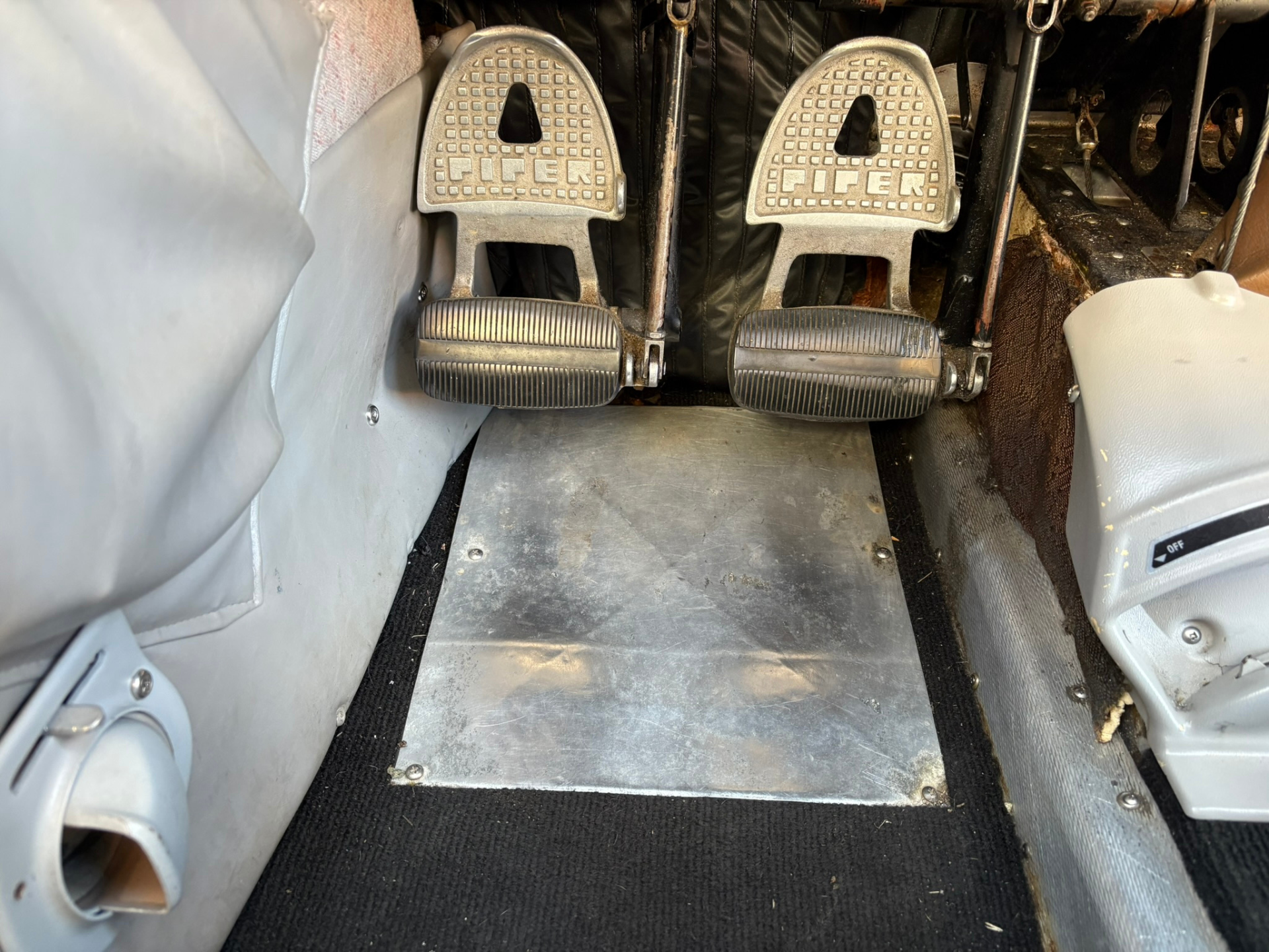 Dual metal Piper rudder pedals with ribbed toe grips mounted on a worn cockpit floor.