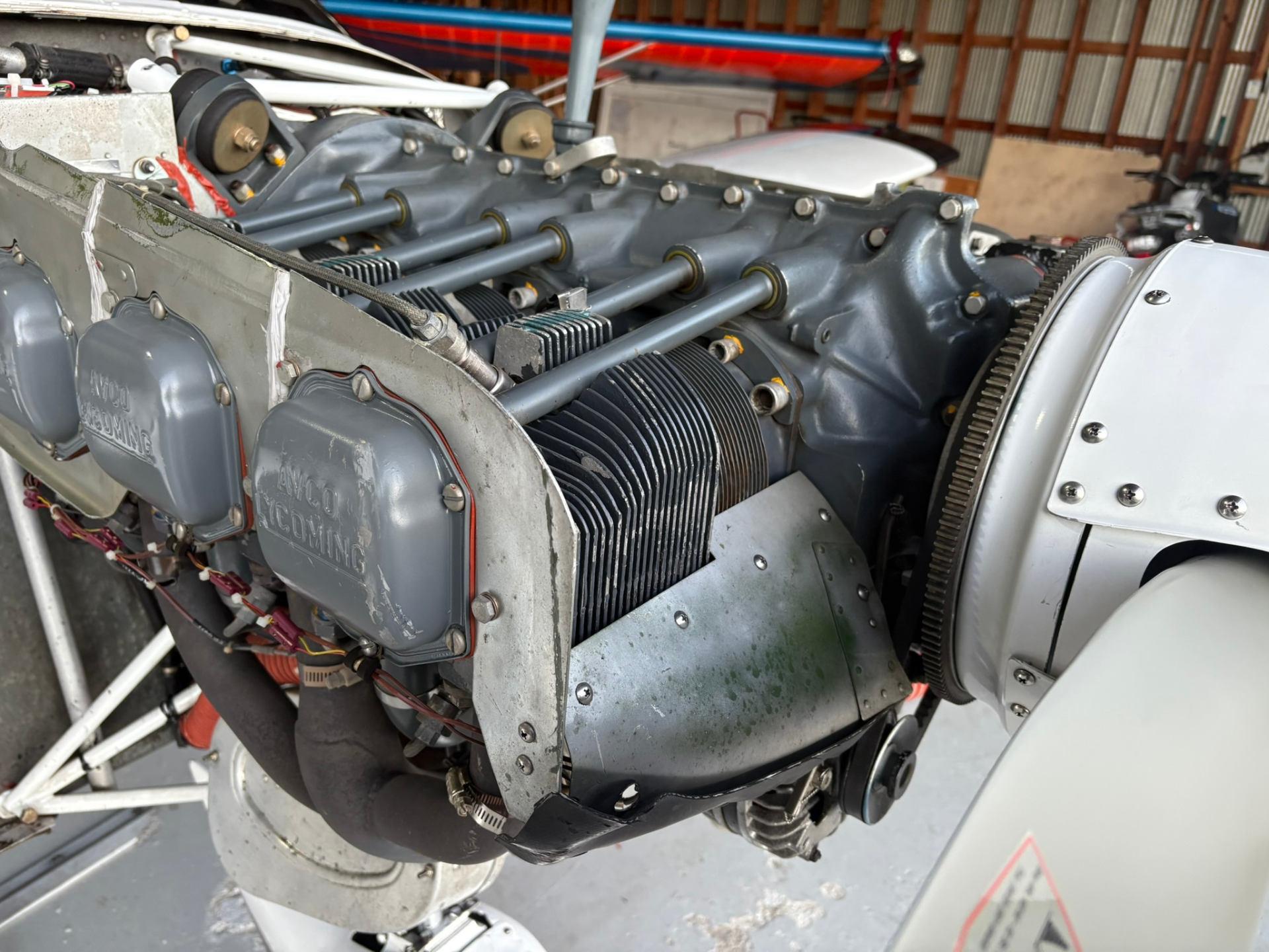 Close-up of an aircraft piston engine with exposed cylinders and mounting plates in a hangar garage setting.