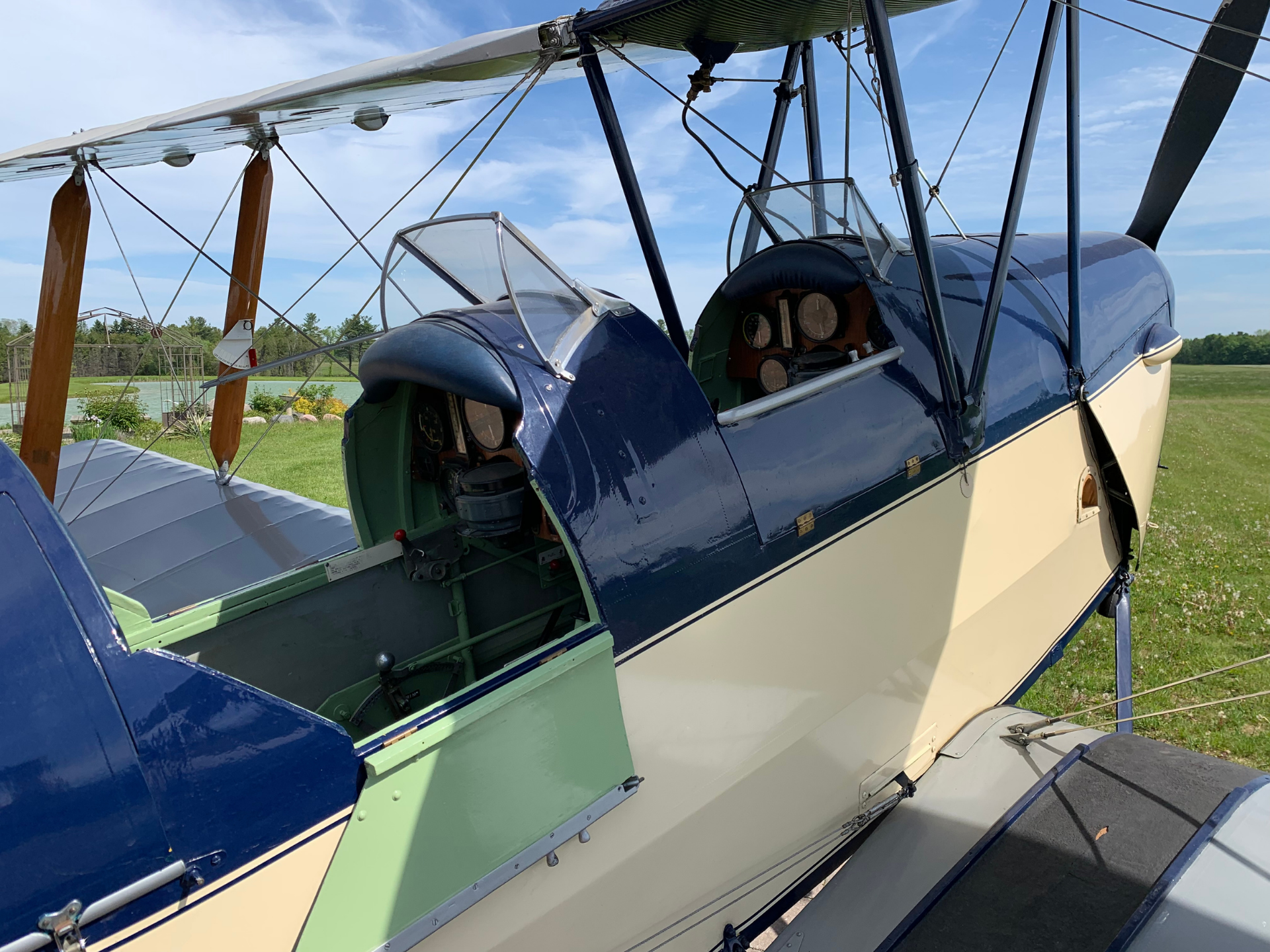 Open cockpit of a vintage blue-and-cream biplane with wooden propeller and exposed instruments inside, on a grassy field.