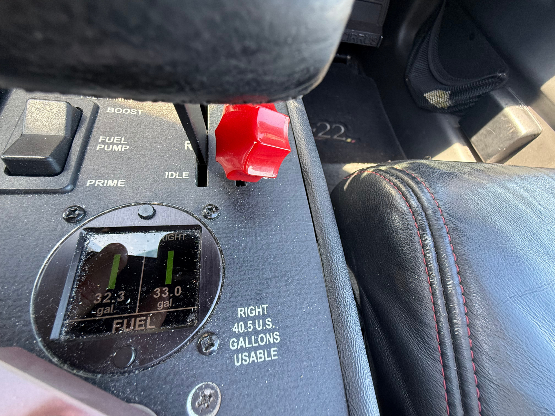 Close-up of an aircraft cockpit console with a red fuel selector/knob, labeled PRIME and IDLE, surrounded by gauges and switches, and black leather nearby.