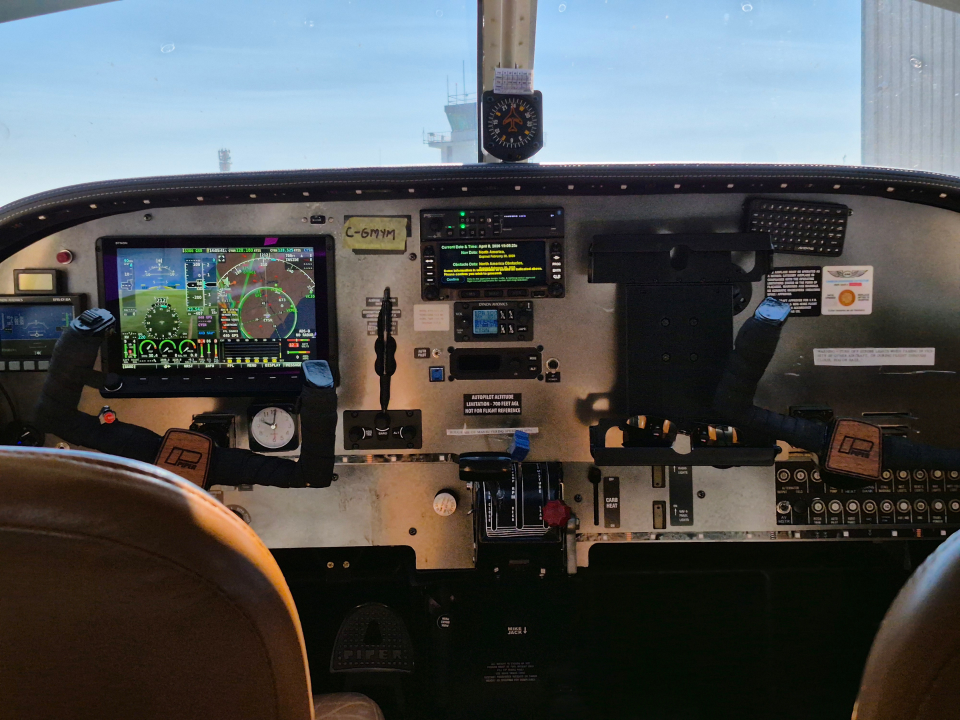 Front cockpit view of a small airplane showing digital avionics displays, control yoke, and pilot seat edges.