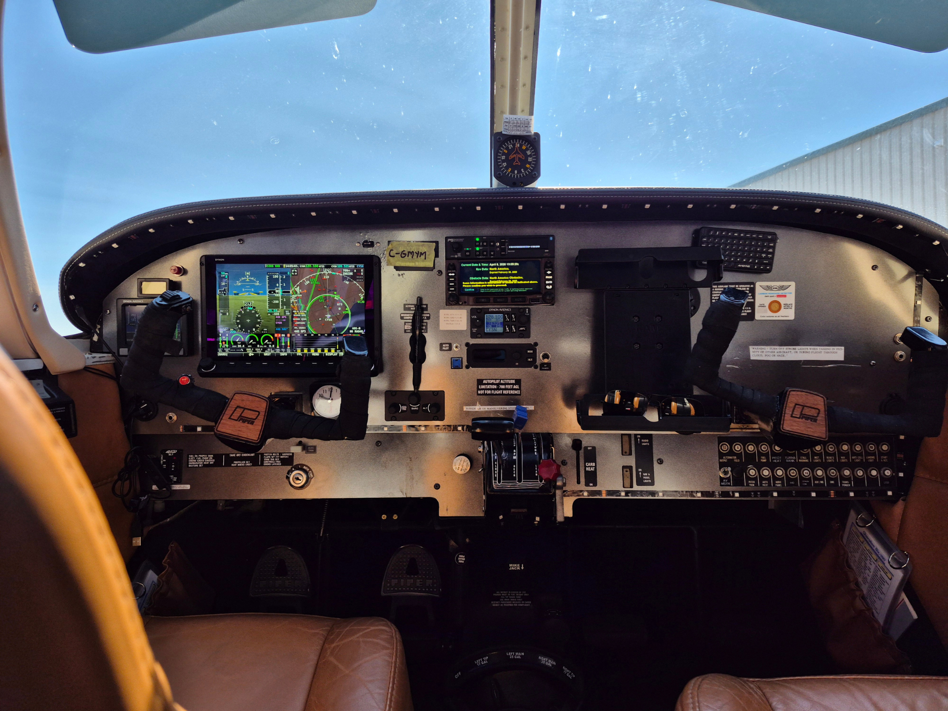 Cockpit view of a small aircraft with flight instruments, yoke, and panels, blue sky visible through windshield.