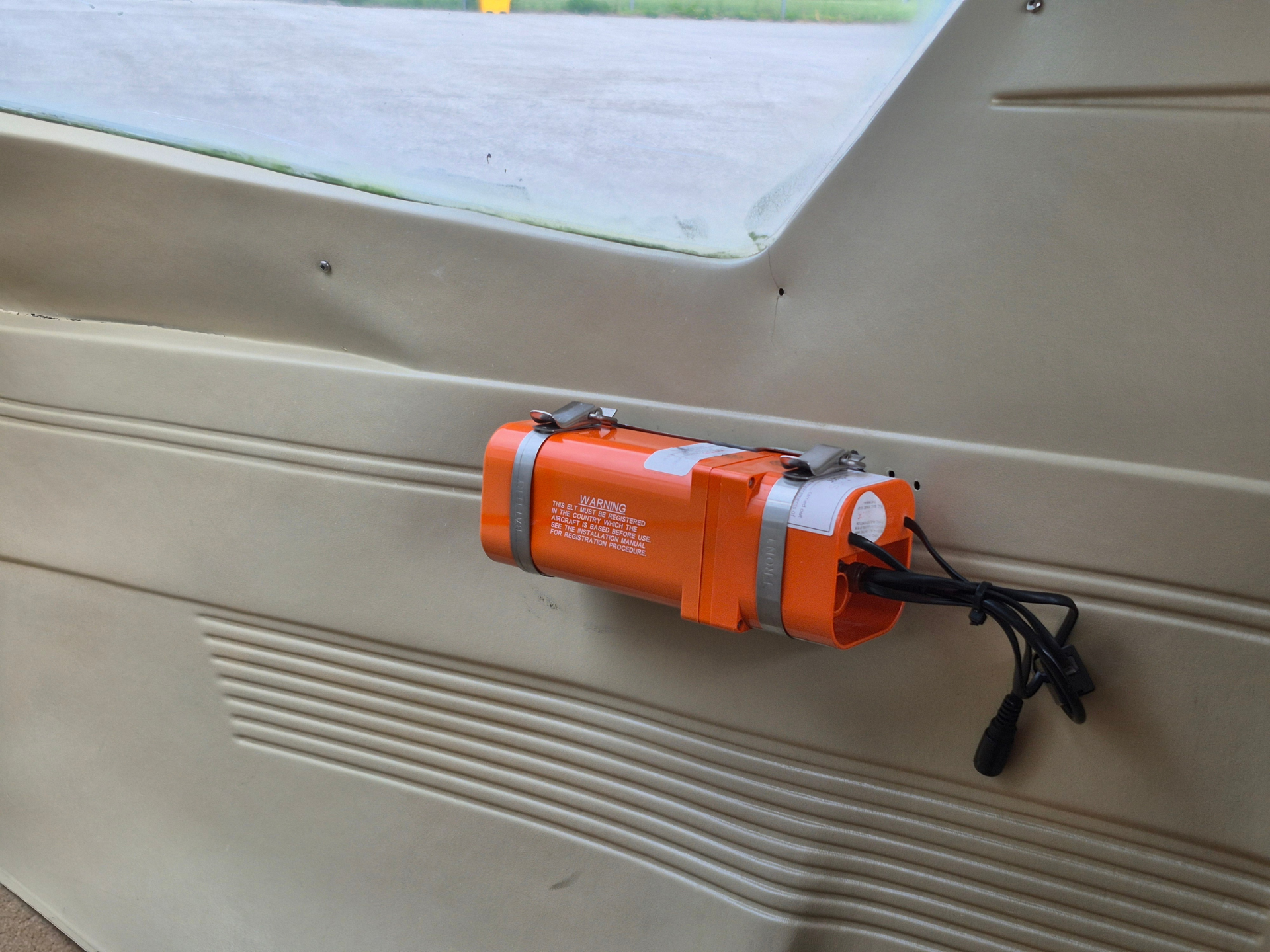Orange emergency flotation/life-raft canister mounted to a beige interior wall with black cords hanging below.