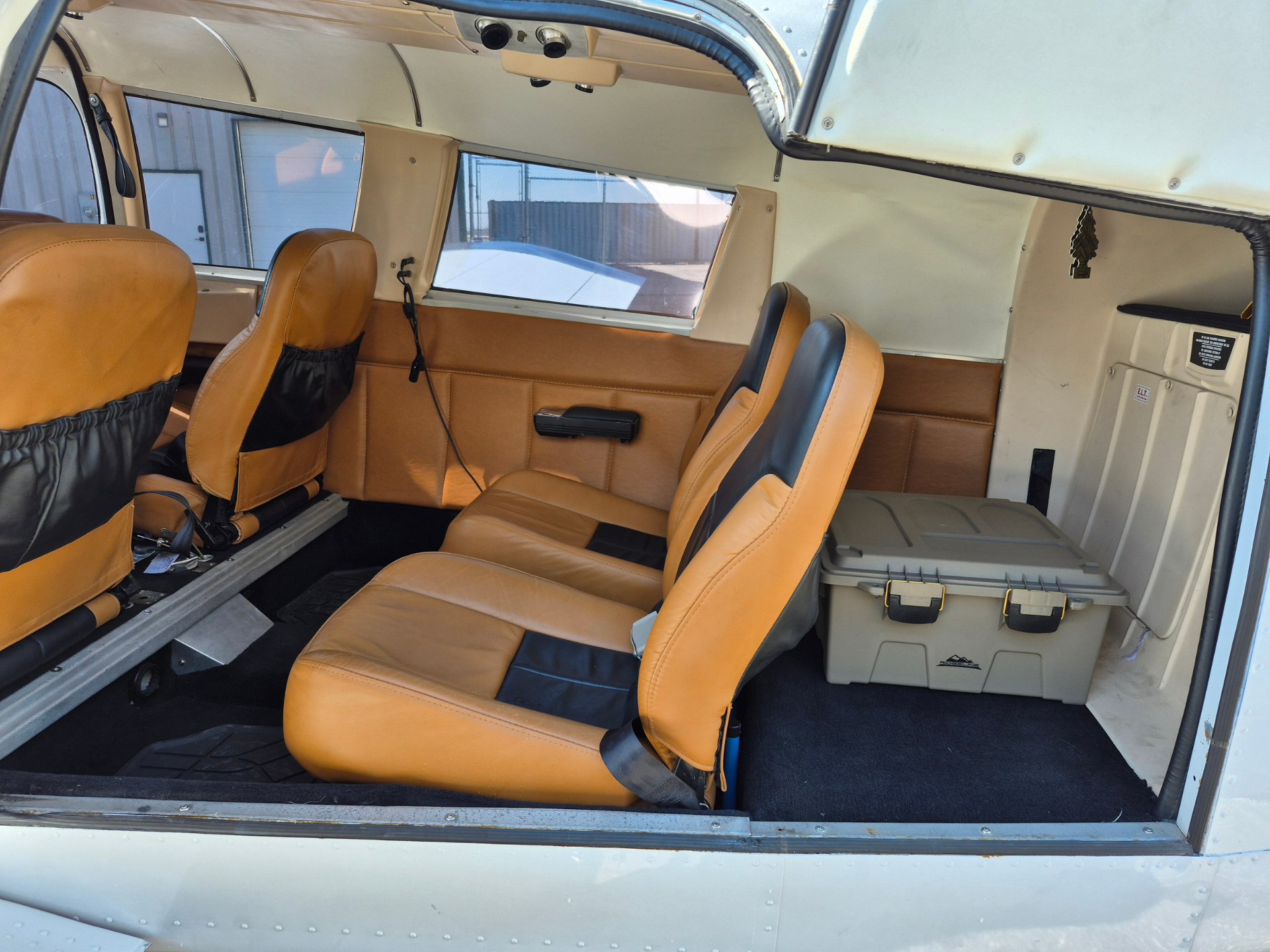 Inside a small aircraft cabin with tan leather seats and a gray storage bin at the rear.