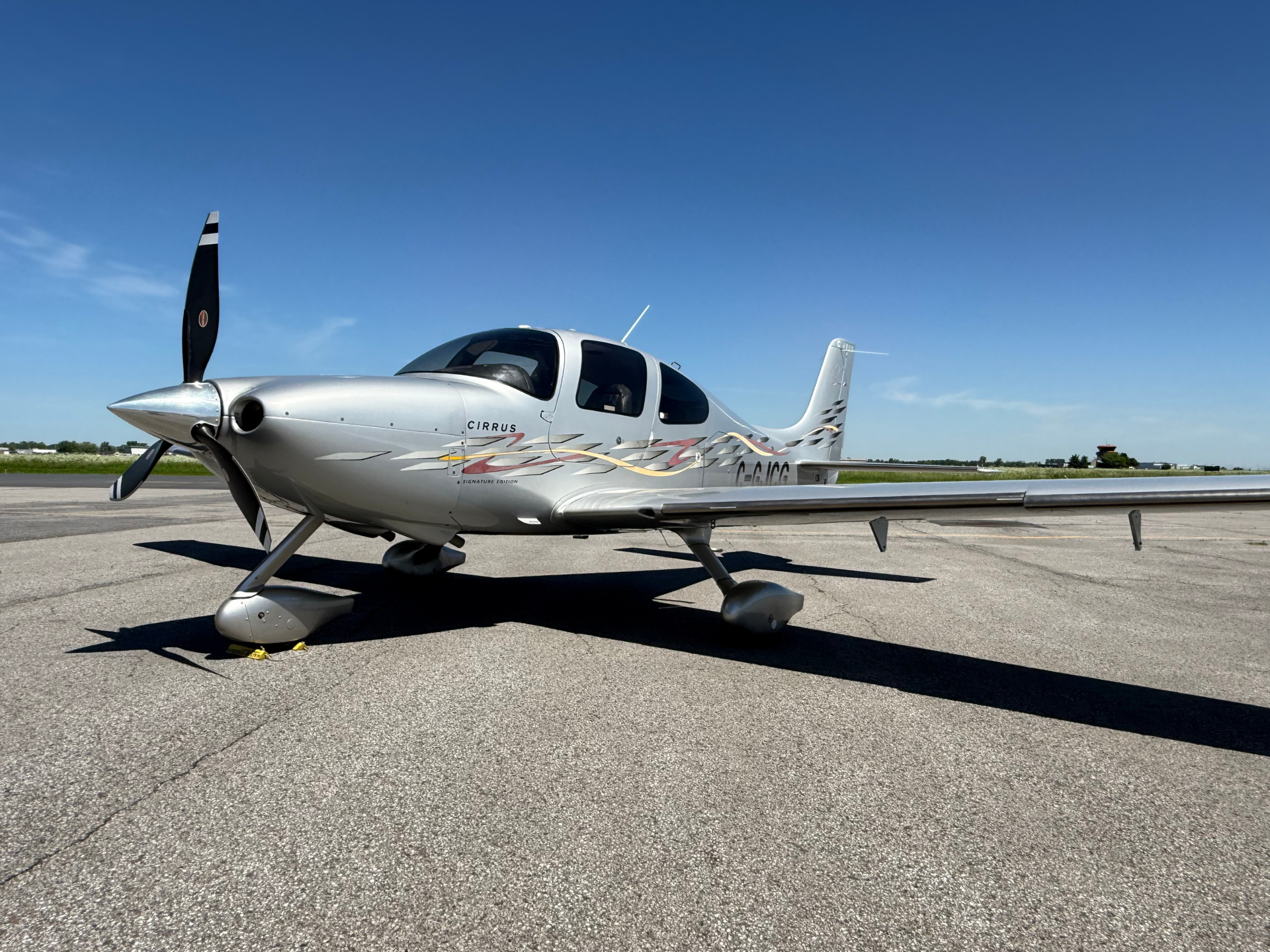 Silver Cirrus private airplane parked on a sunny tarmac with a clear blue sky above.