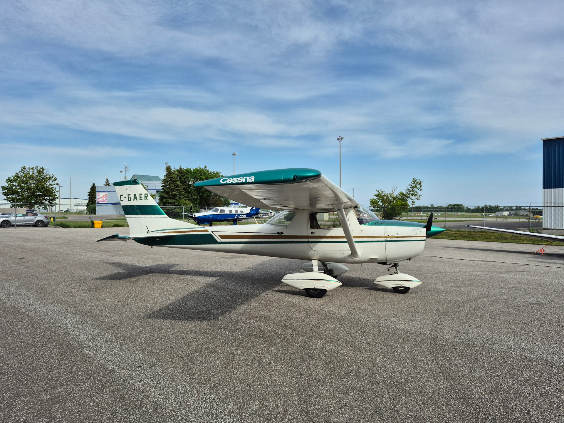 Small white and teal Cessna airplane parked on an airport tarmac with a blue sky above.