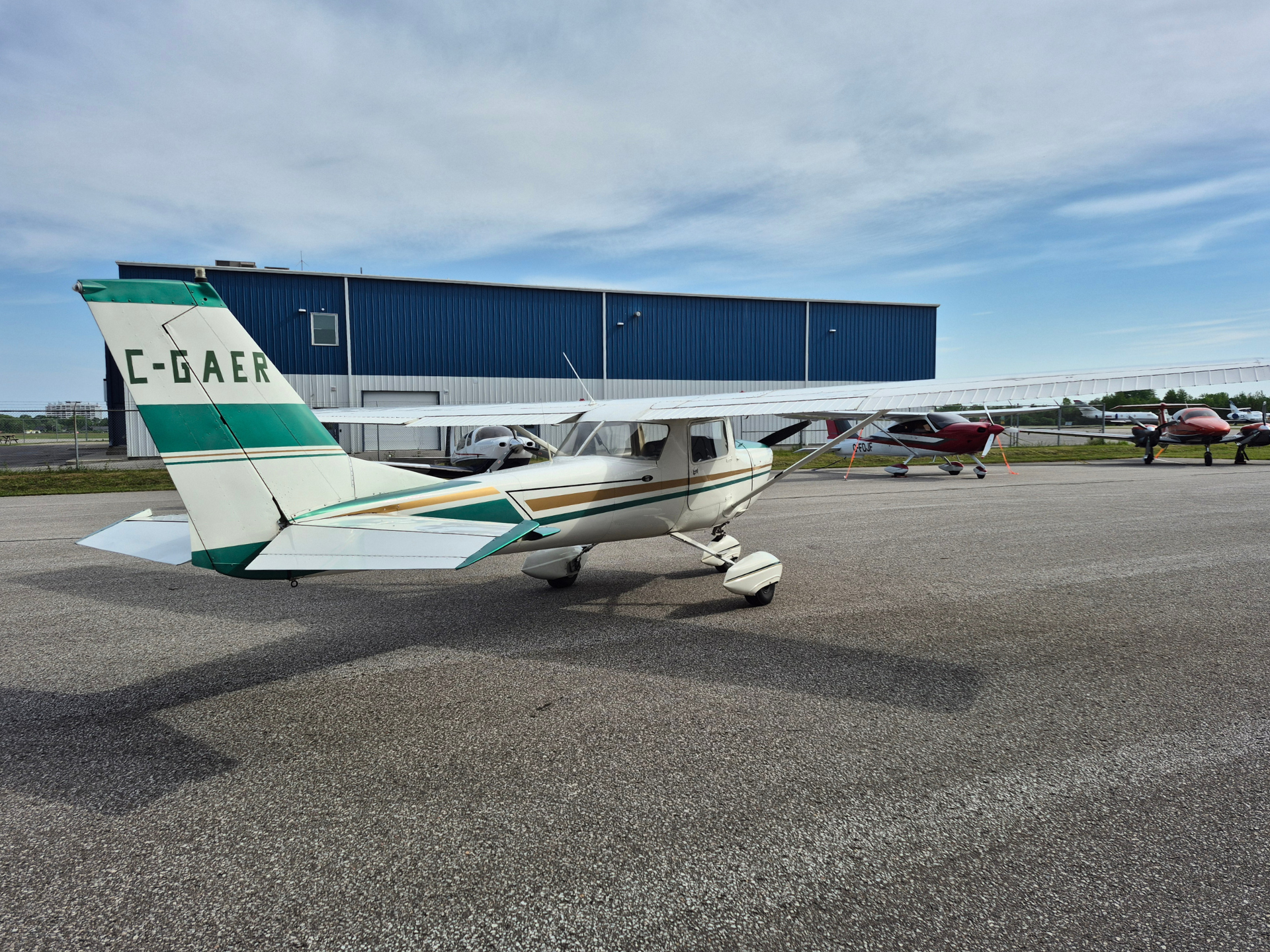Small white and teal airplane parked on a tarmac with a blue hangar behind.