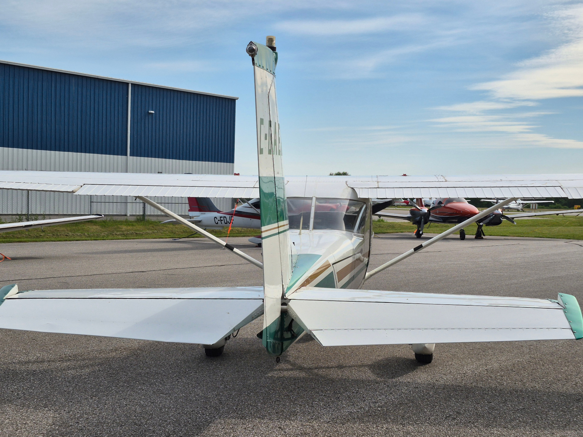 Small single-engine airplane viewed from behind on a runway with a blue hangar in the background; tail and wings centered, clear sky above.