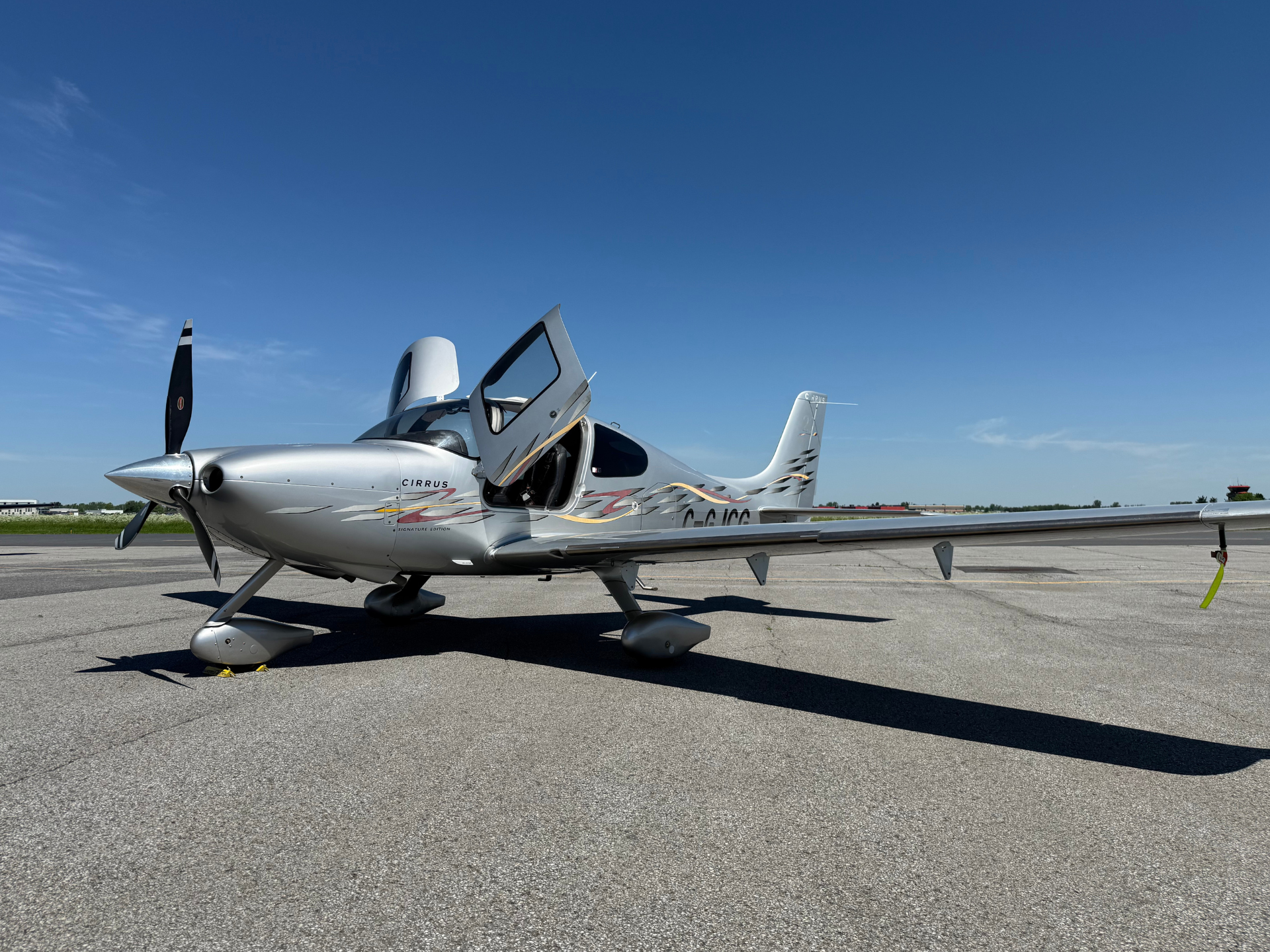 Silver small airplane parked on an airport tarmac with its door open under a clear blue sky.