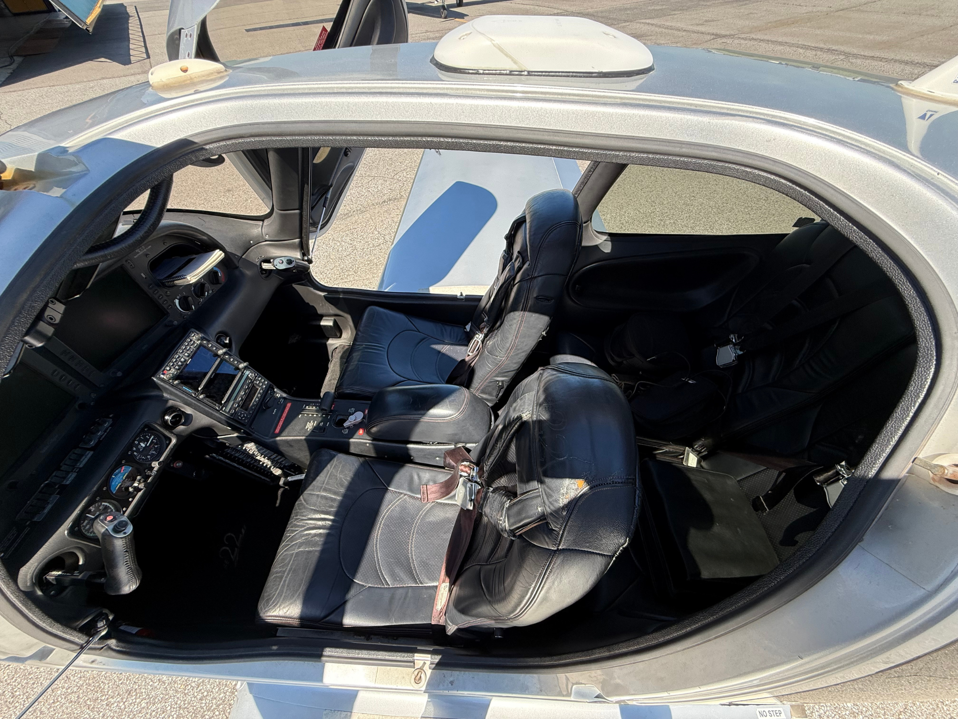 Cockpit view of a small airplane with two black leather seats, instrument panel, and open door, parked on the tarmac.