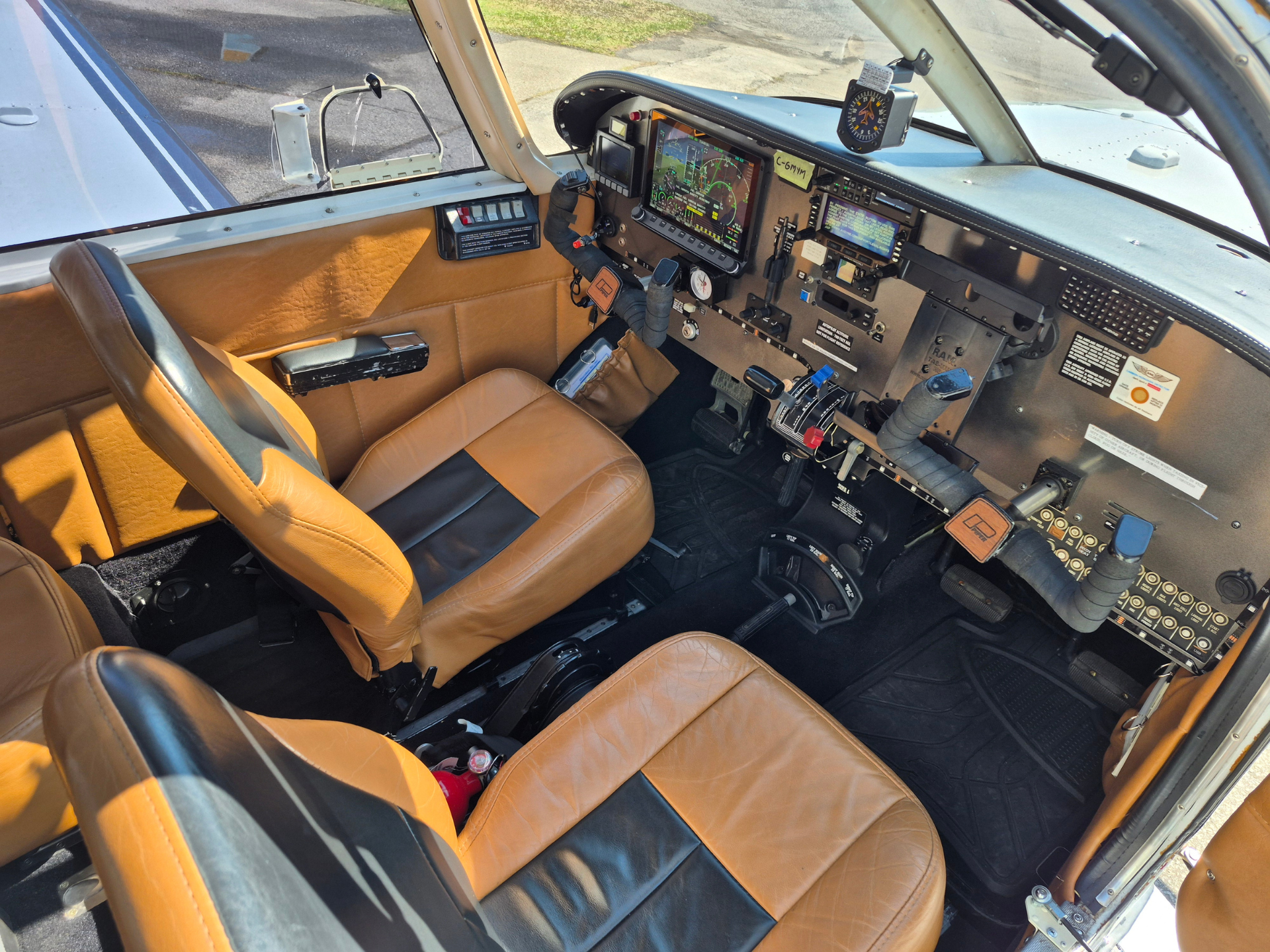 Interior view of a small aircraft cockpit with tan leather seats, a control yoke, and instrument panels near the windshield.