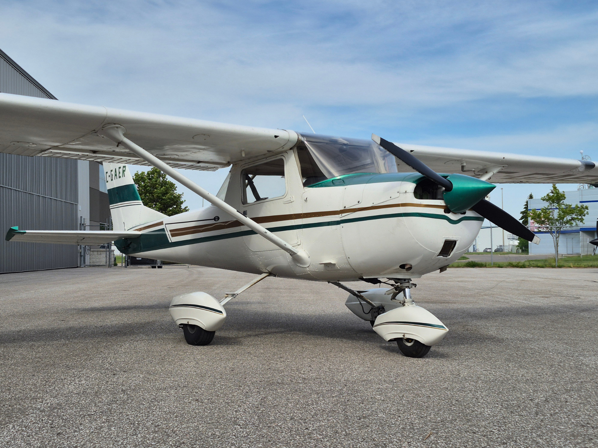 Small propeller airplane parked on a tarmac beside a hangar, tail number C-GAER, with white and teal livery.