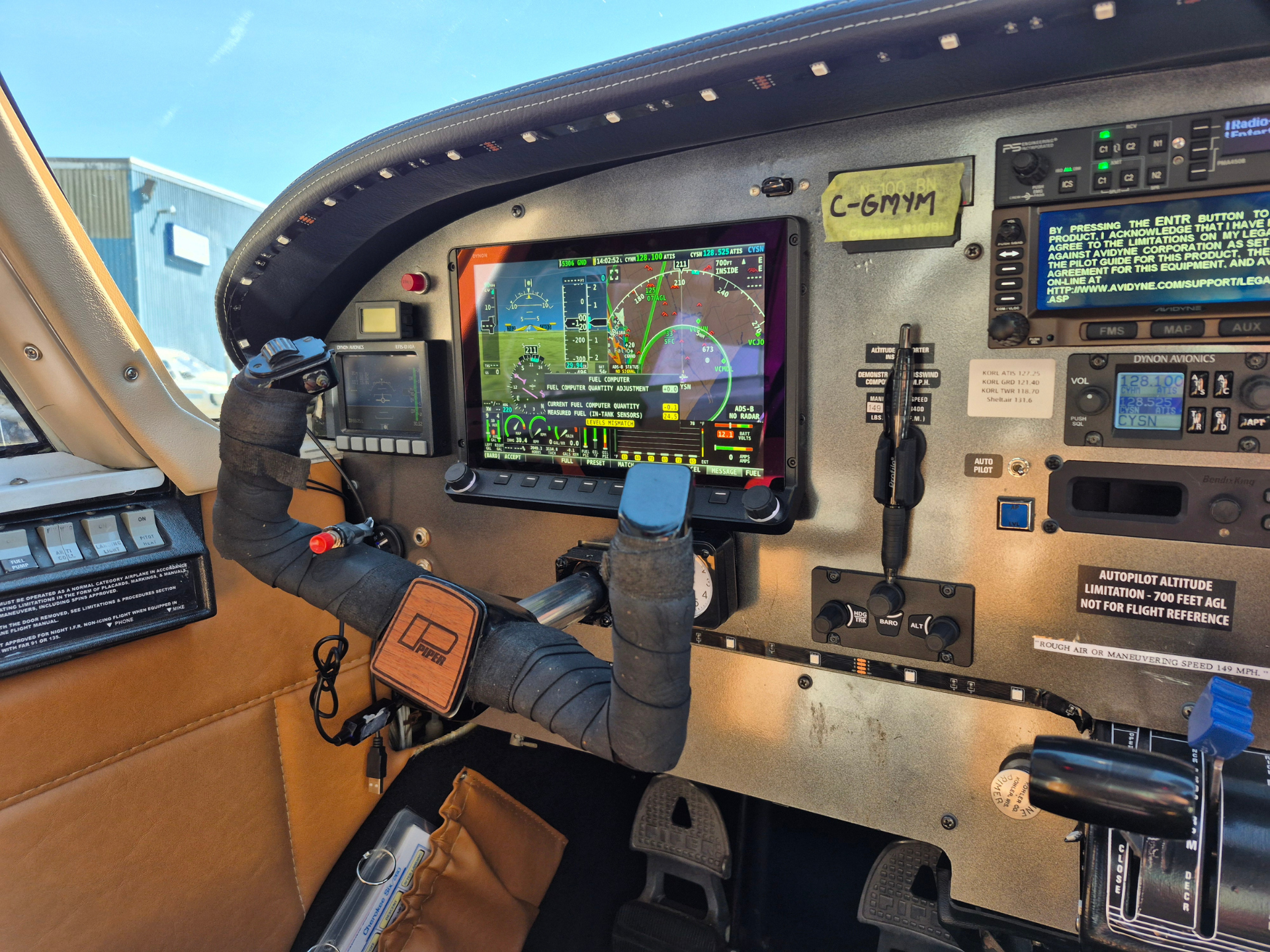 Close-up of a small aircraft cockpit with a digital flight display, yoke, and various switches in view.