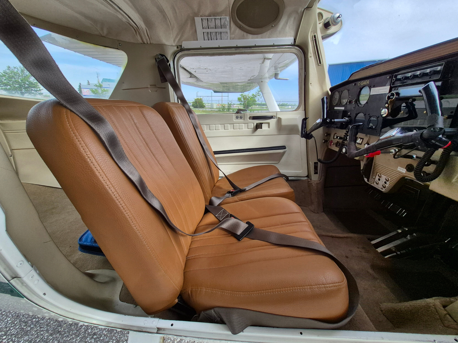 Cockpit of a small airplane with brown leather seats and a seatbelt, visible controls on the right and an open door view ahead.