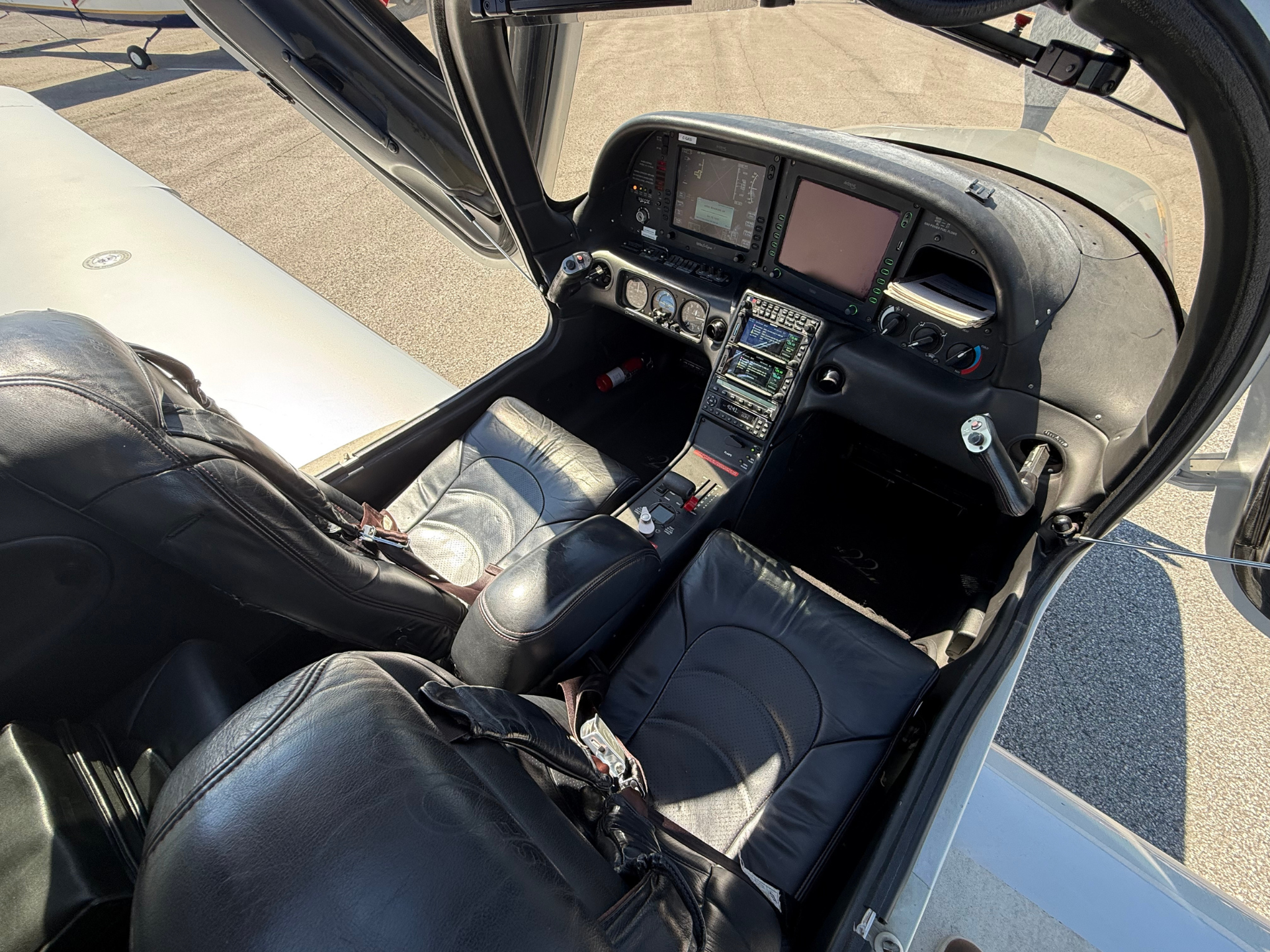 Interior of a small airplane cockpit with two large screens and leather seats, door open to the left.