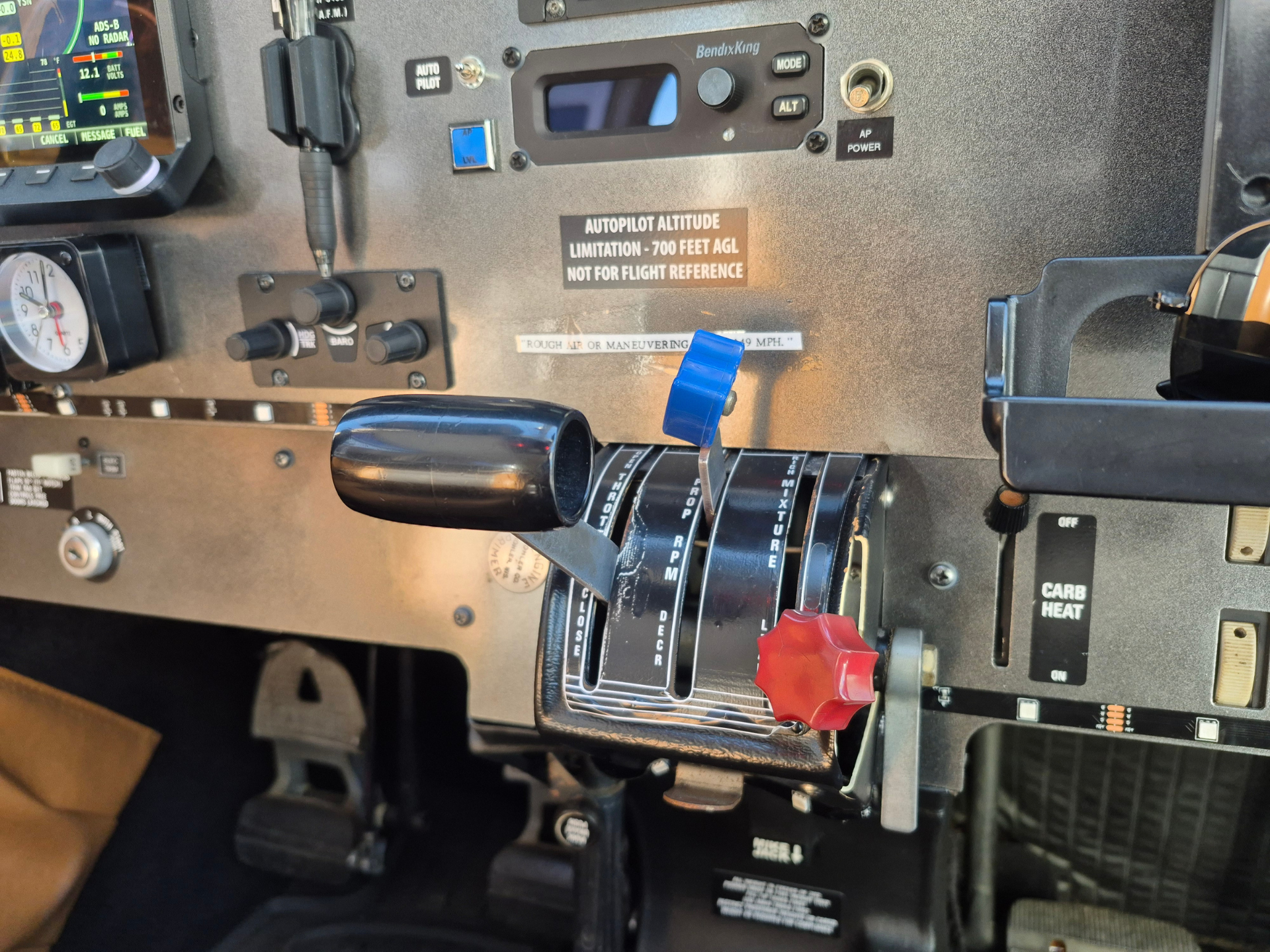 Cockpit panel with throttle levers and autopilot controls; blue and red knobs, gauges, and warning labels.