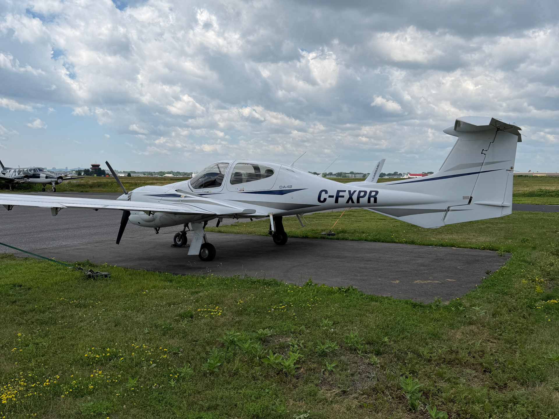 Small white single-engine airplane parked on a tarmac, tail number C-FXPR, with a cloudy sky above and grassy foreground.