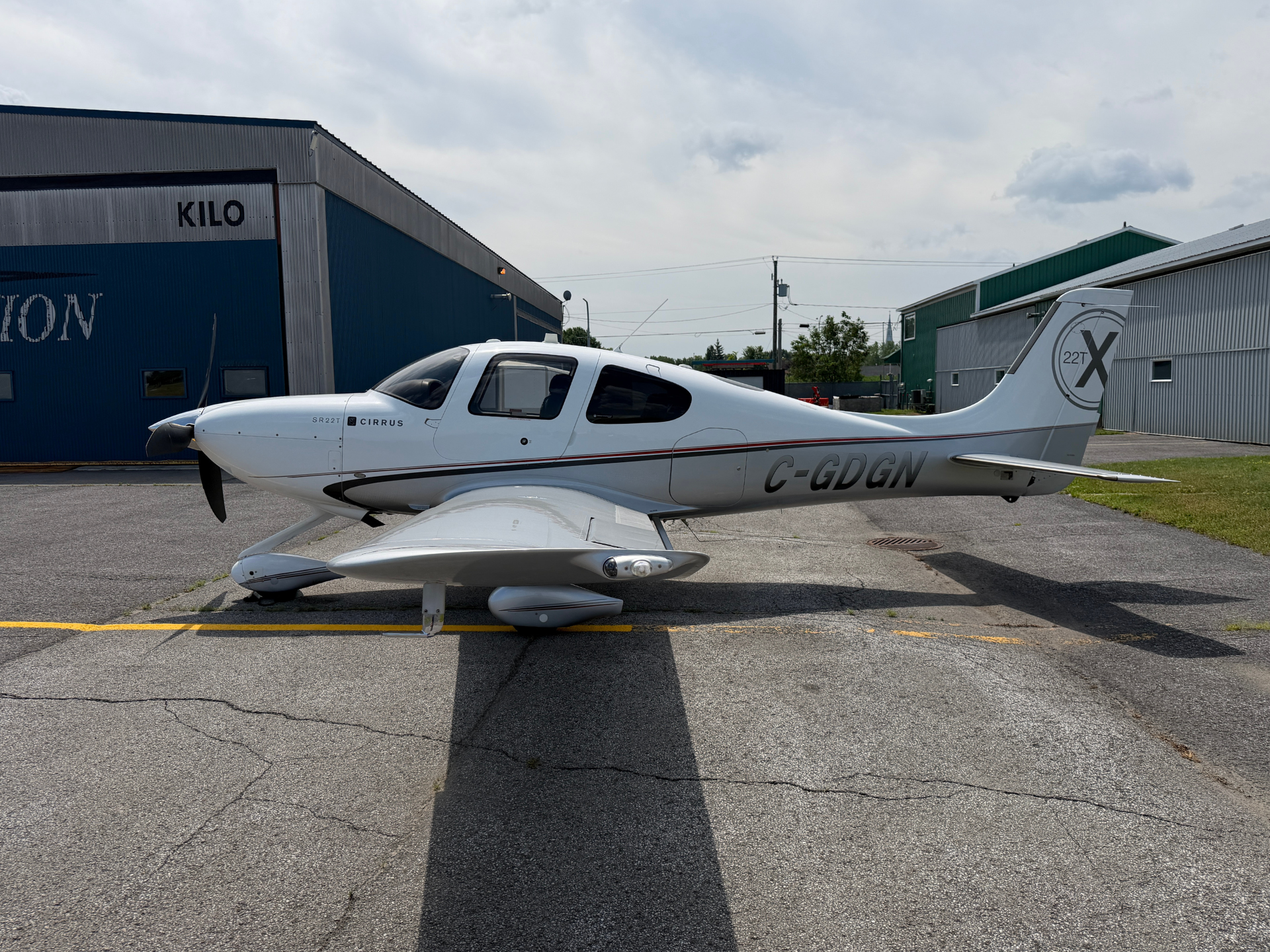 White Cirrus SR22 parked on the tarmac beside blue and green hangars.