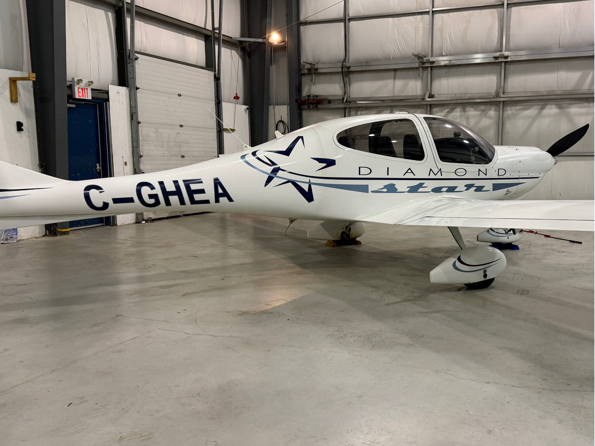 White Diamond aircraft inside a hangar, blue logo and registration C-GHEA visible along the fuselage, propeller at the nose.