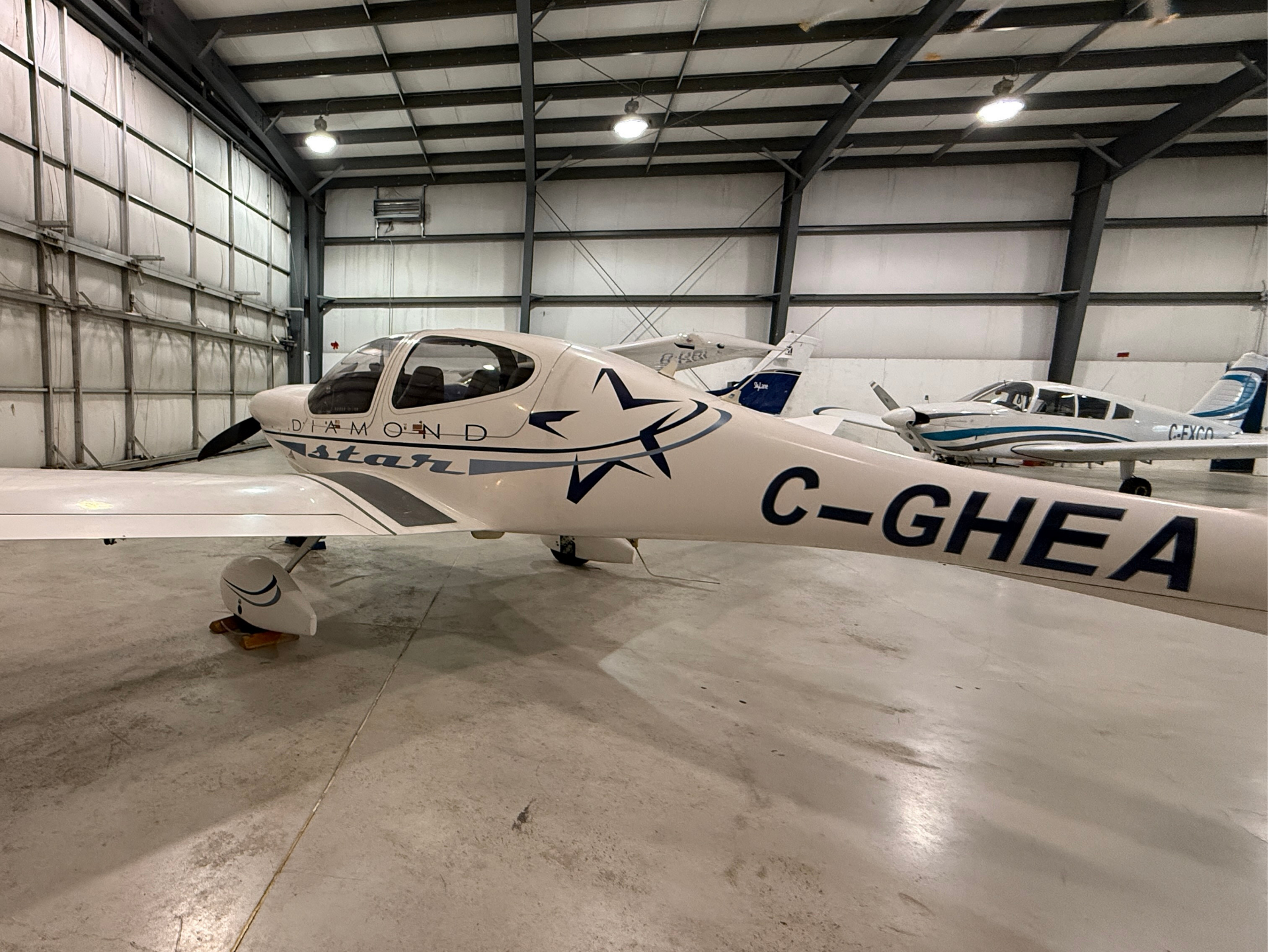 White Diamond aircraft parked inside a hangar, blue graphics on fuselage and registration C-GHEA visible.