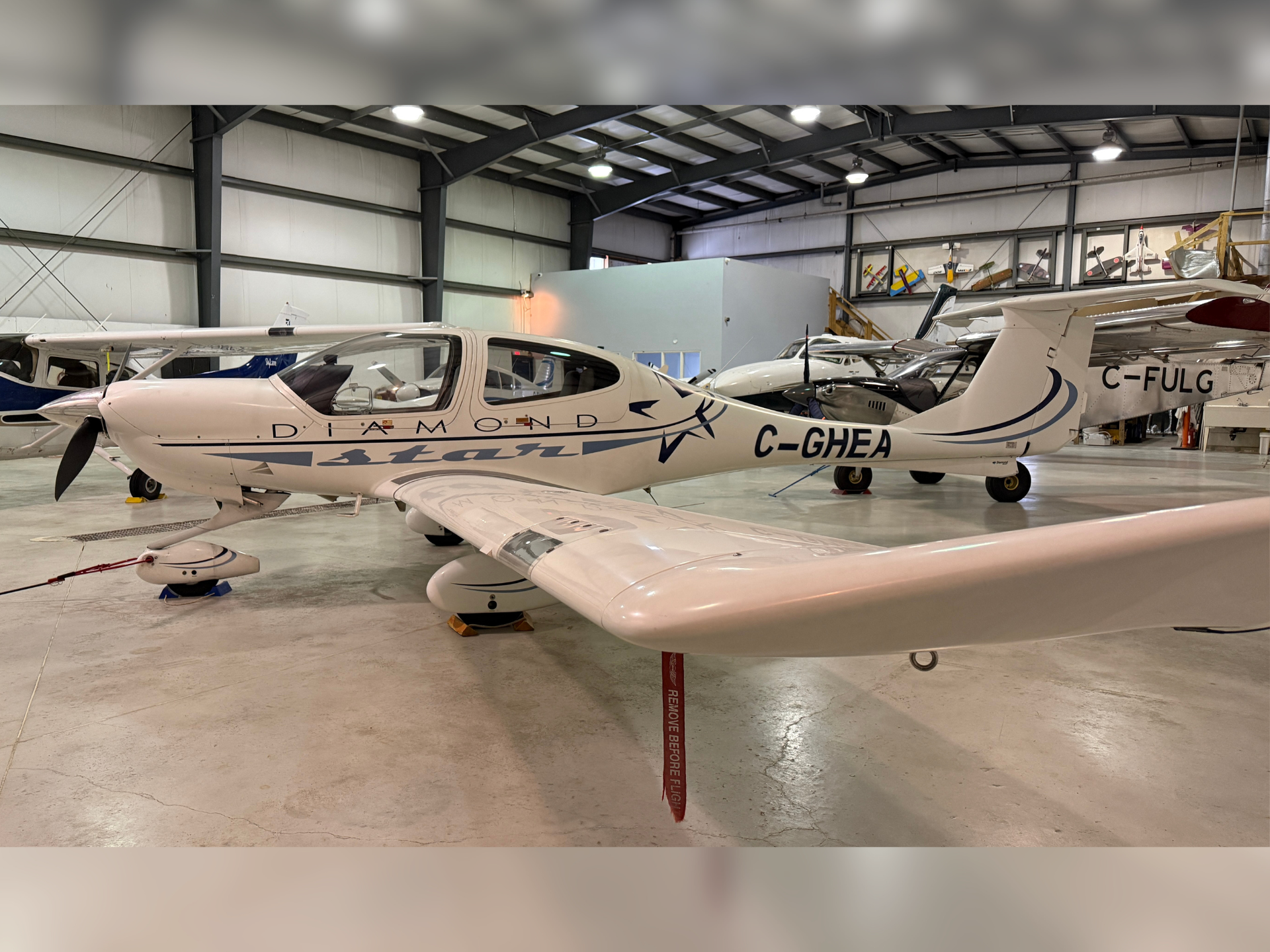 White Diamond Aircraft light airplane inside a spacious hangar with other small planes in the background; registration C-GHEA visible on fuselage.