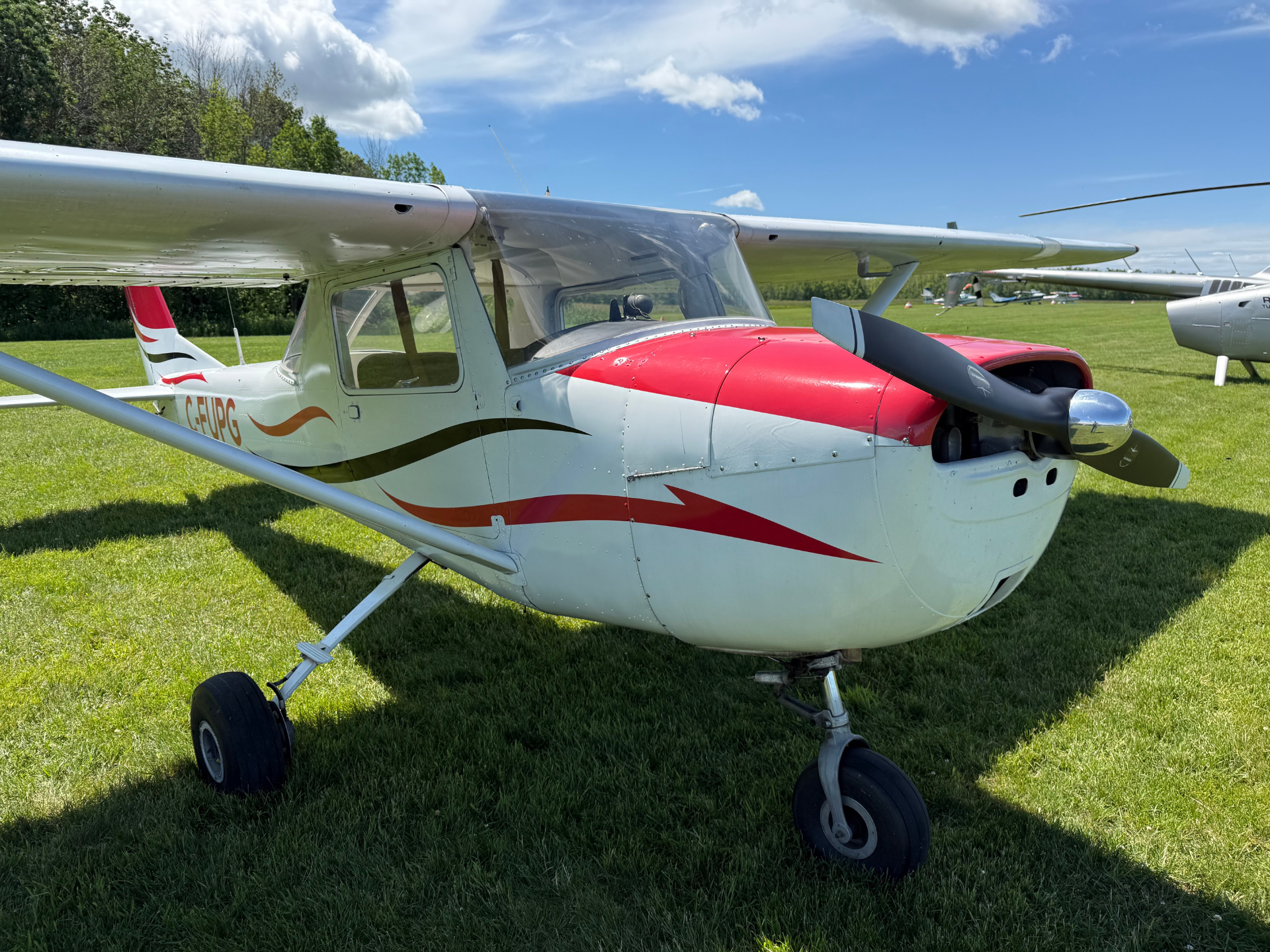 Small single-engine propeller airplane parked on a grassy airfield, white with red and orange graphics.