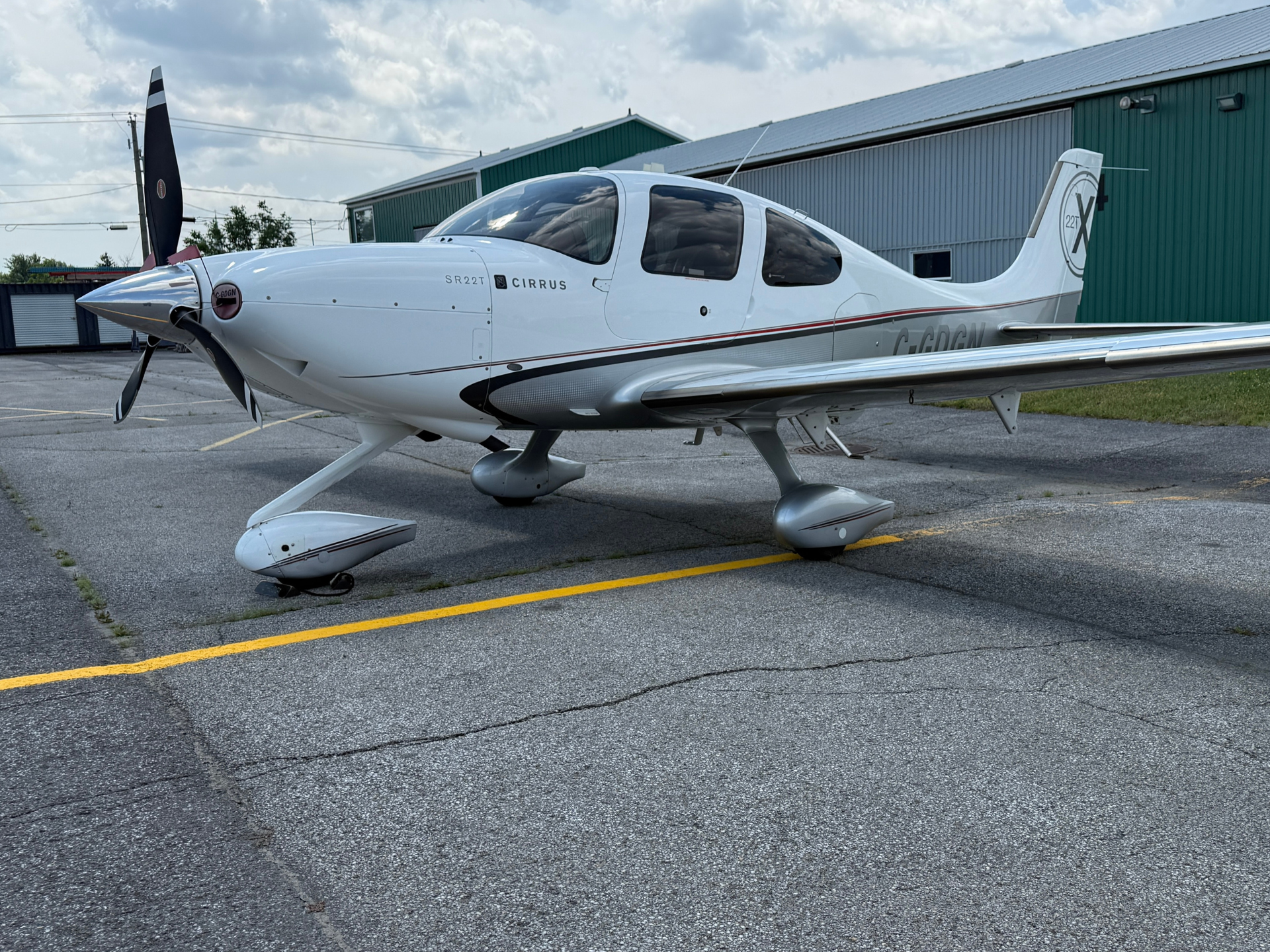 White Cirrus SR22T small aircraft parked on a tarmac beside a green hangar, blue sky above