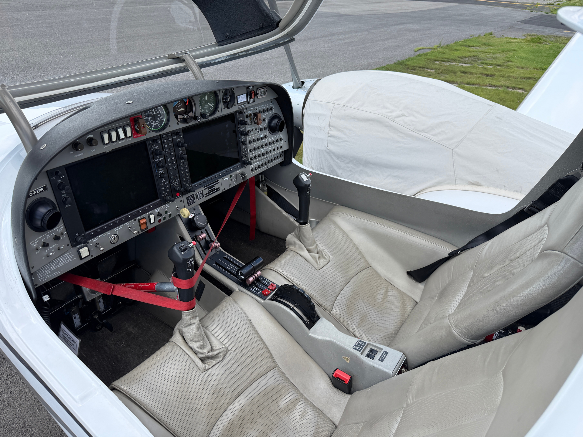 Light aircraft cockpit with dual seats, instrument panel, and red seat belts visible between the controls and screens.