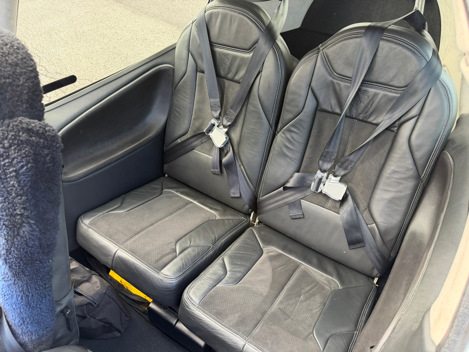 Two black leather car seats with over-the-shoulder seatbelts in a vehicle's rear interior, ready for passengers.