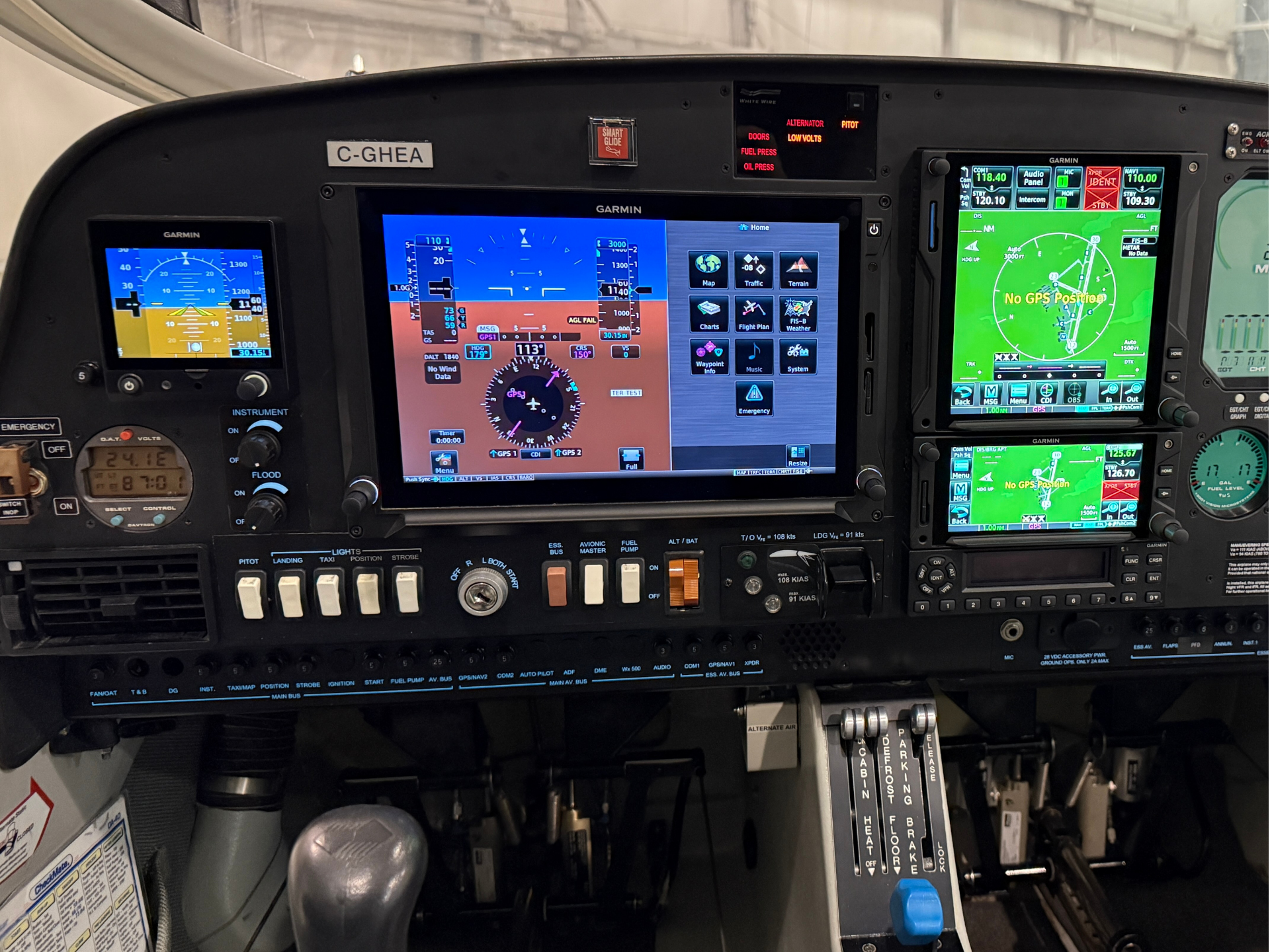 Cockpit instrument panel with multiple Garmin screens displaying flight data and navigation in a small aircraft cabin, including a center primary flight display and right-side map screens.