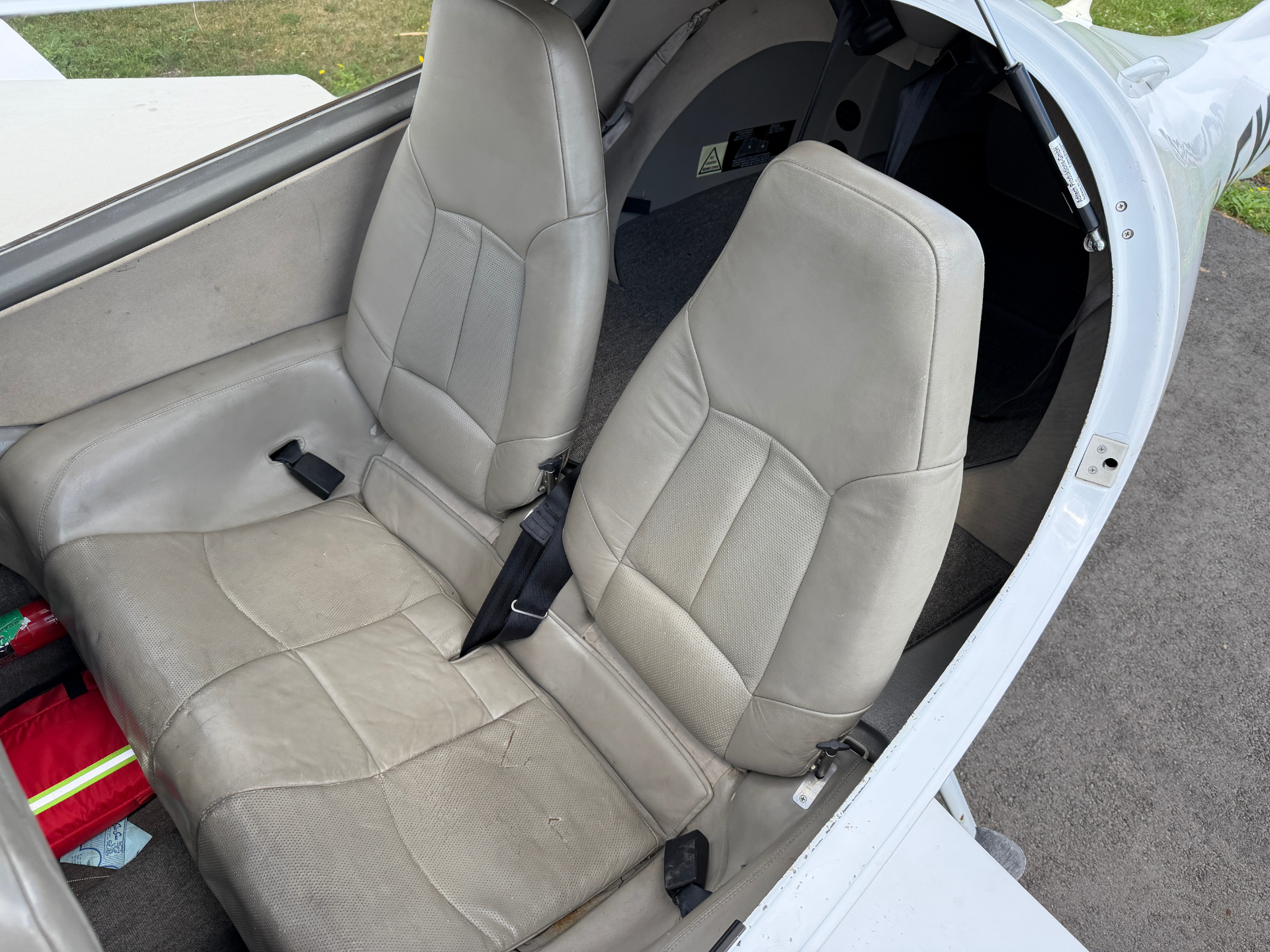 Two beige leather airplane seats with seat belts in a small cockpit, canopy open.
