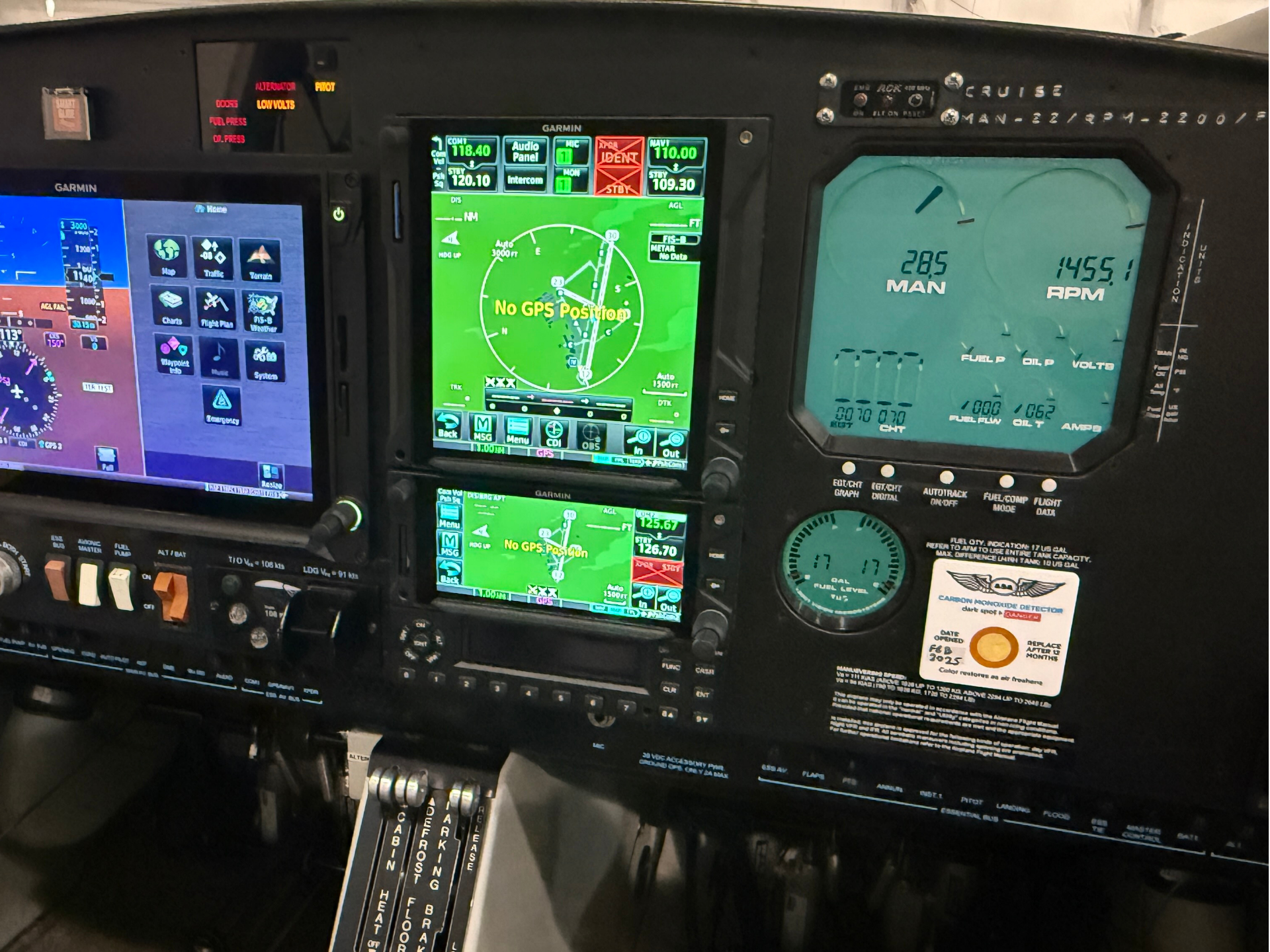 Cockpit instrument panel with three Garmin screens; central green navigation map shows 'No GPS Position' while other screens display flight data and systems information. Below are throttle pedals and switches.
