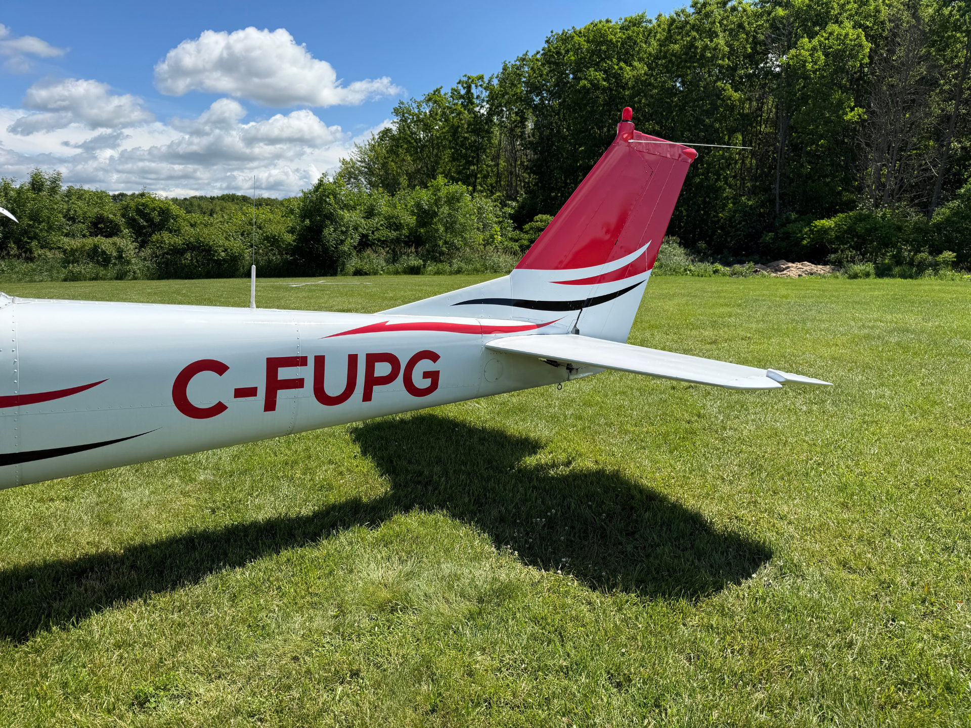 Tail section of a small white aircraft on a grassy airfield, red and white livery with C-FUPG registration visible.