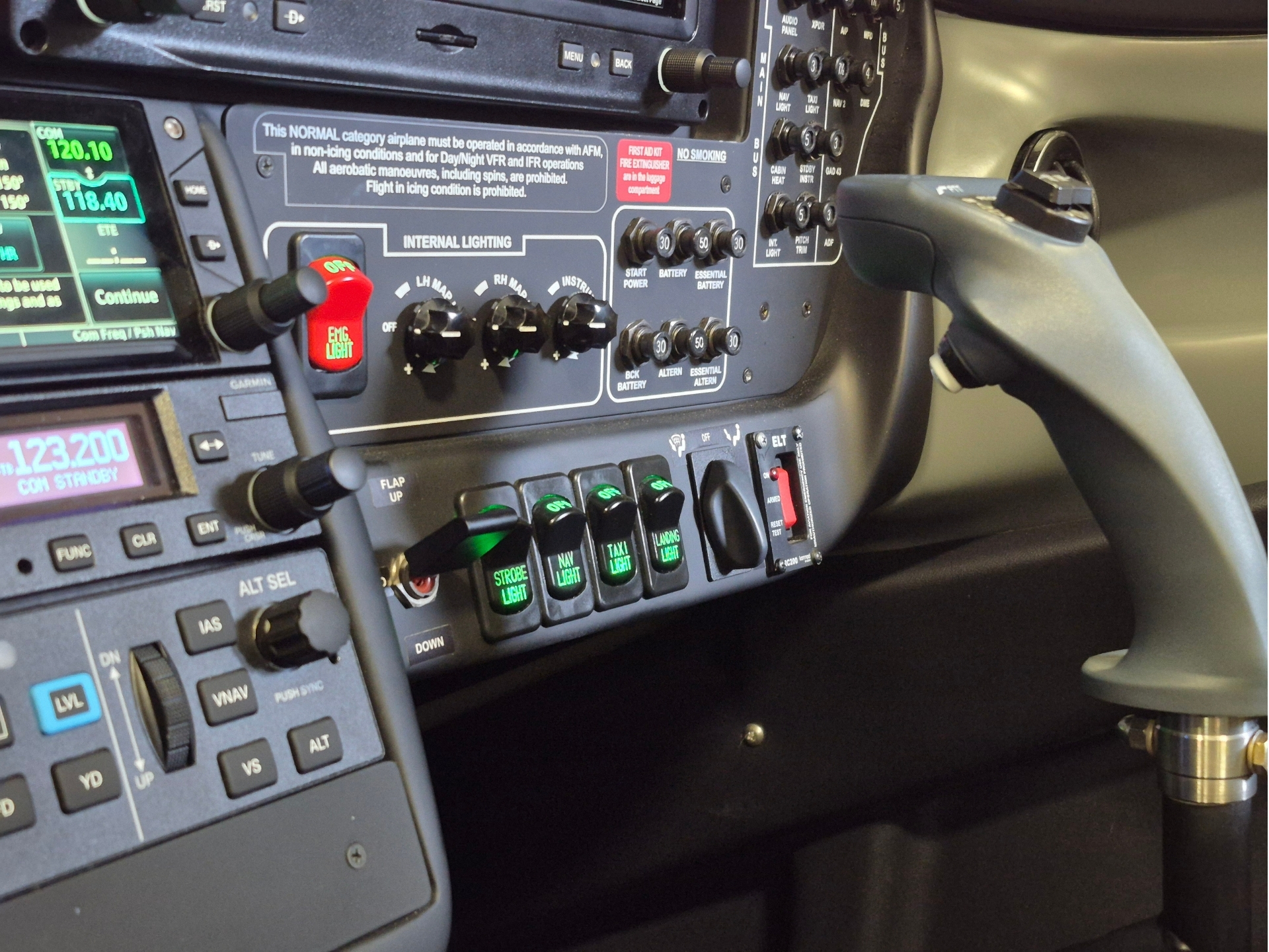 Aircraft cockpit instrument panel with multiple digital displays, labeled switches, and controls including throttle lever on the right side, inside a cabin cockpit.