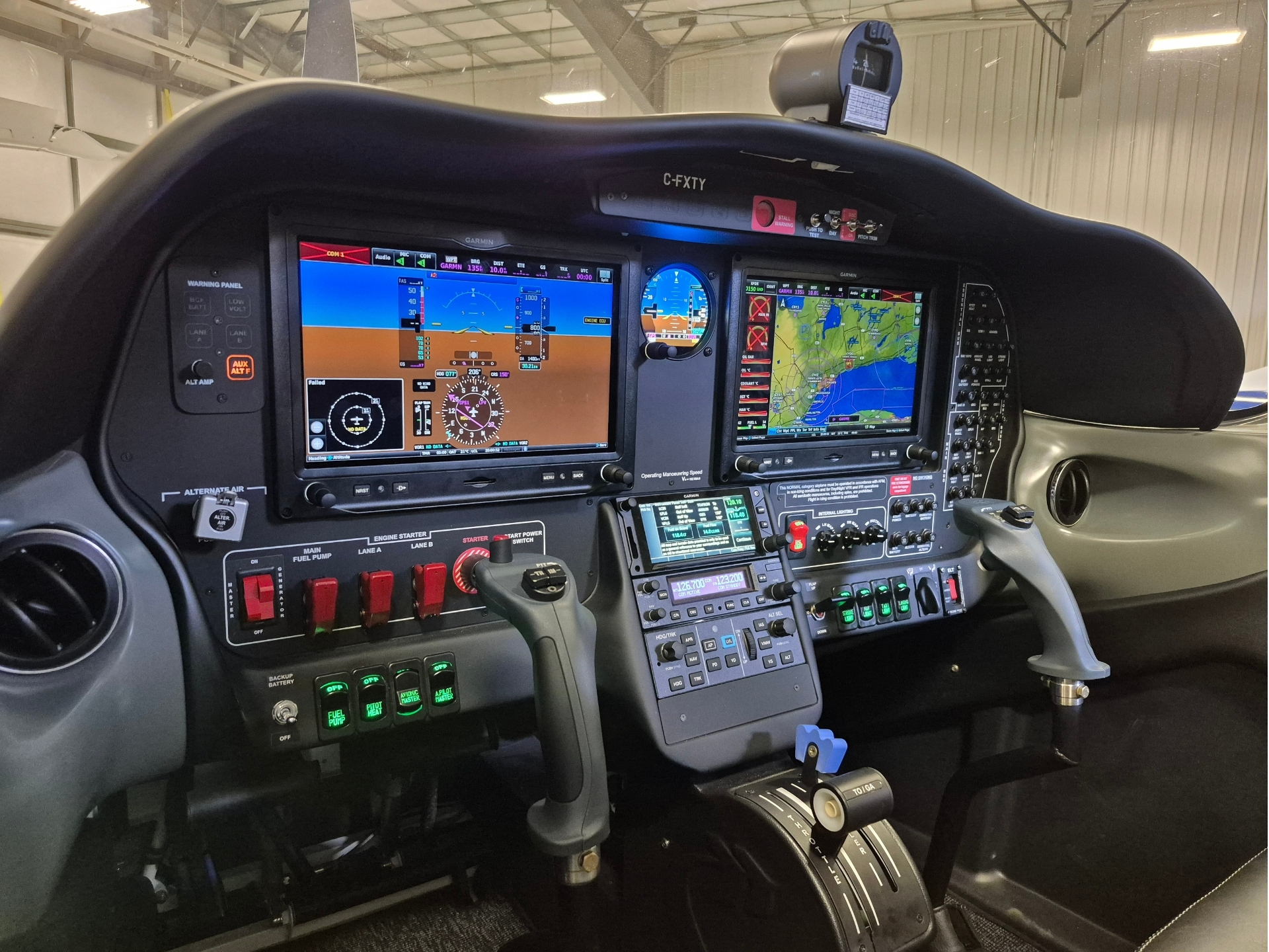 Small aircraft cockpit with two Garmin glass screens, throttle levers, and flight controls.