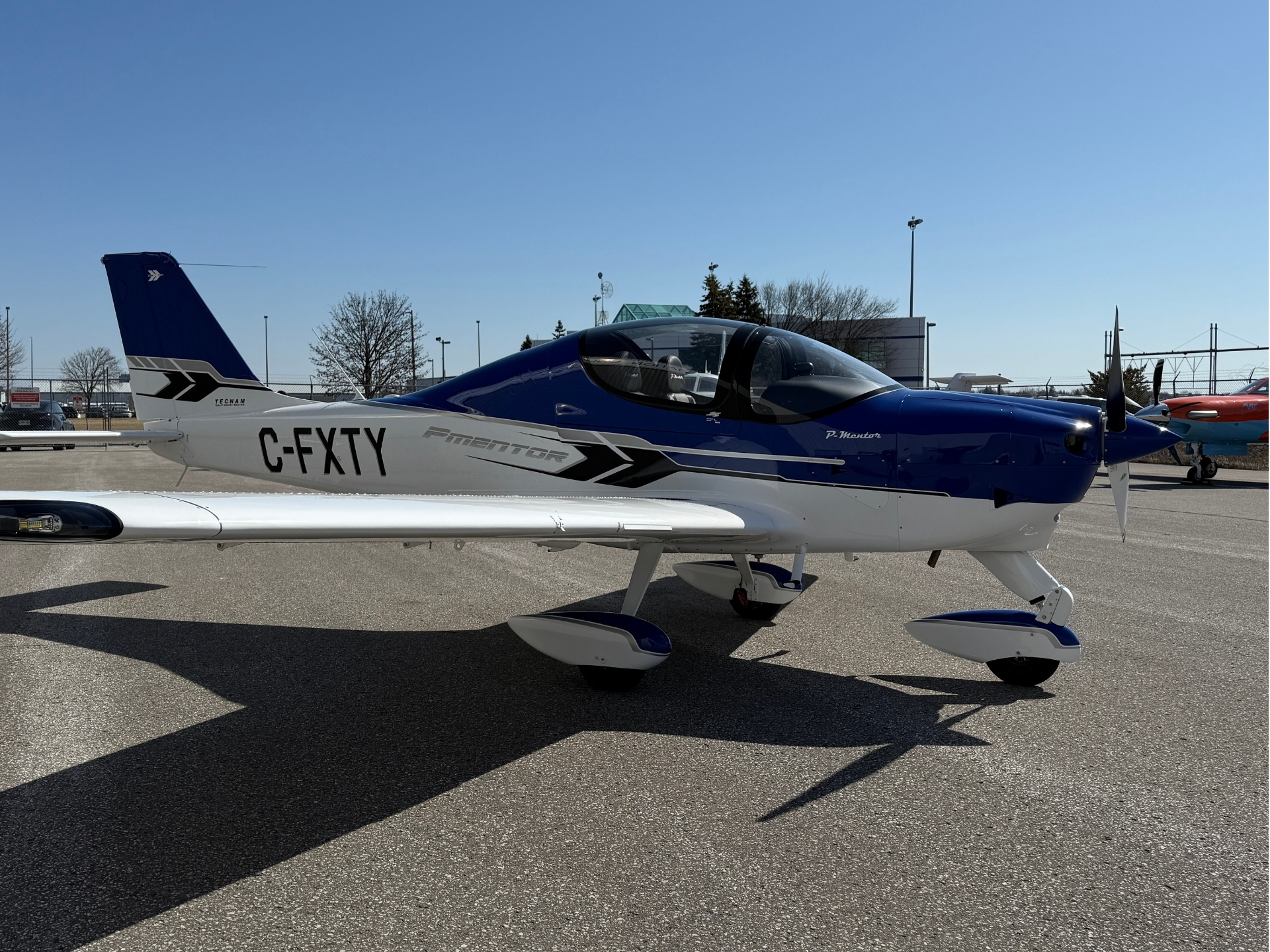 Blue and white single-engine airplane parked on a sunny tarmac, tail number C-FXTY visible on the fuselage.