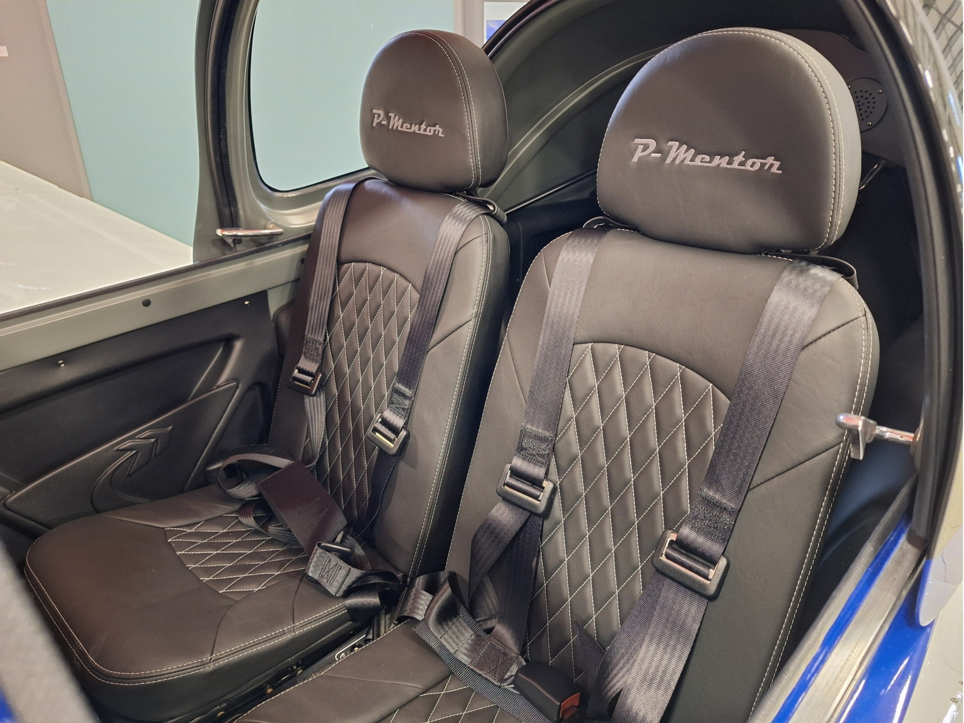 Two black leather car seats with diamond stitching and gray seat belts inside a blue vehicle.
