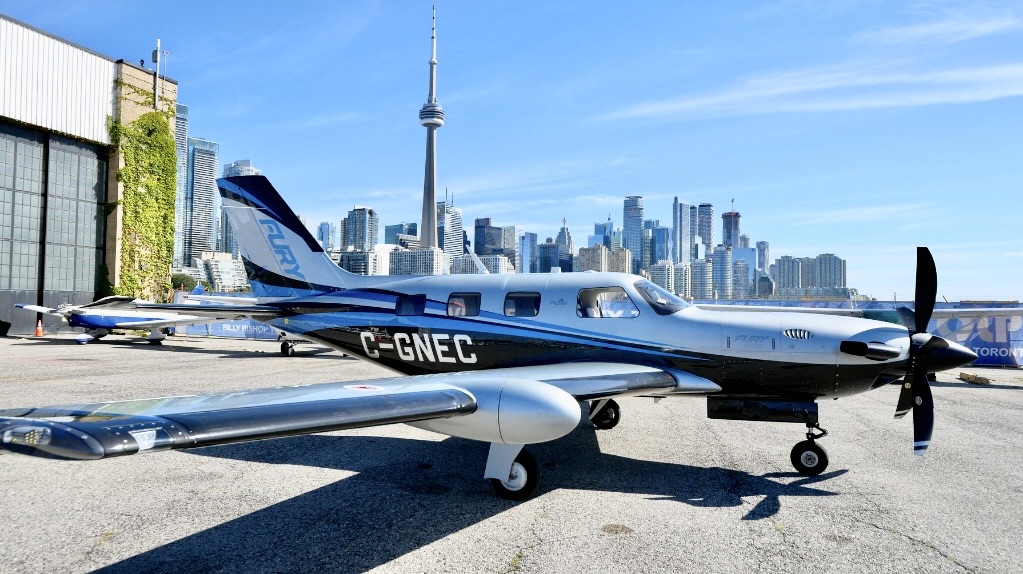 Blue and white single engine propeller plane parked on a tarmac with the Toronto skyline and CN Tower behind itthe aircraft registration G GNEC visible on the fuselage