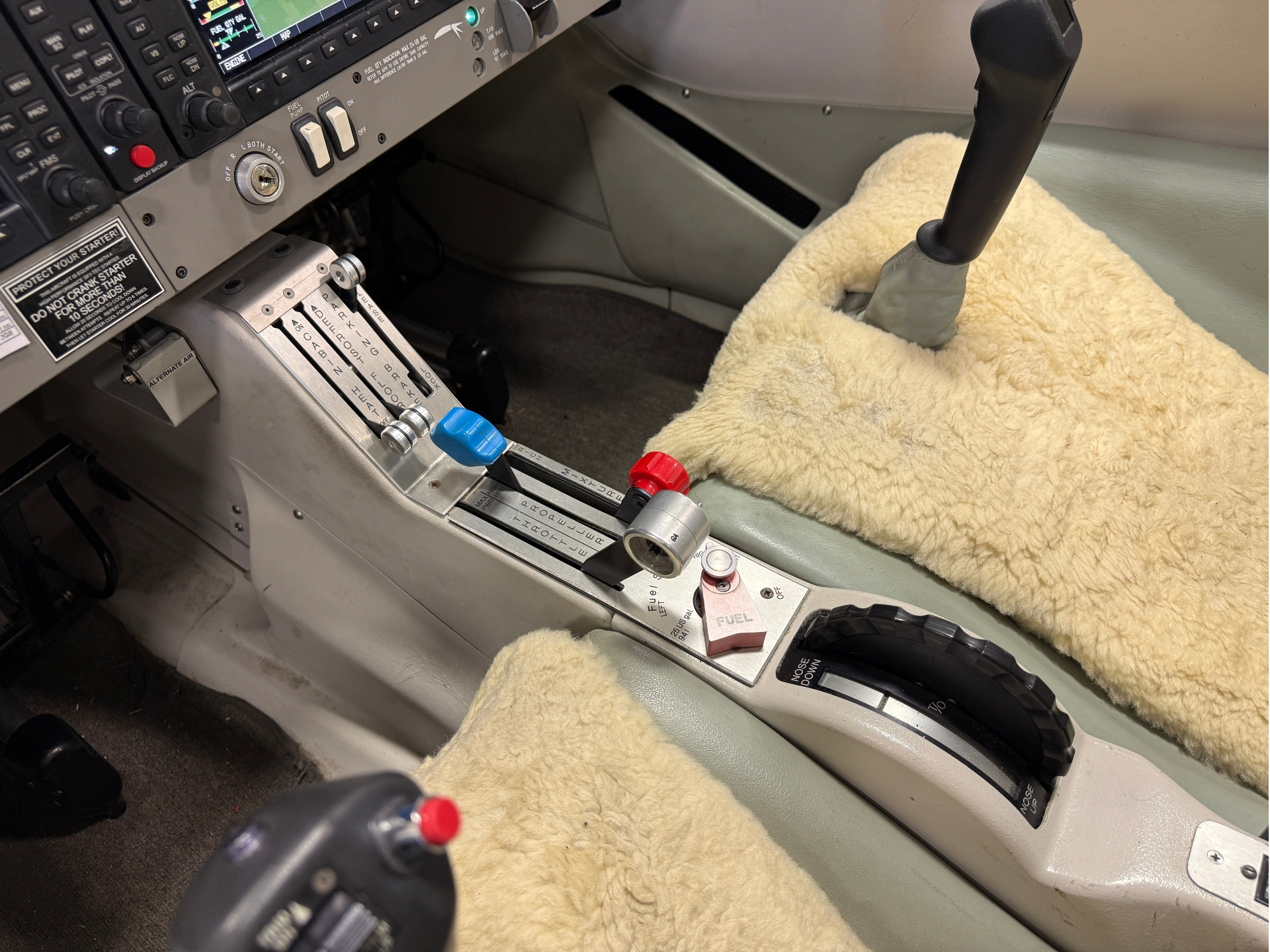 Cockpit interior with throttle levers and control panels covered in beige sheepskin.