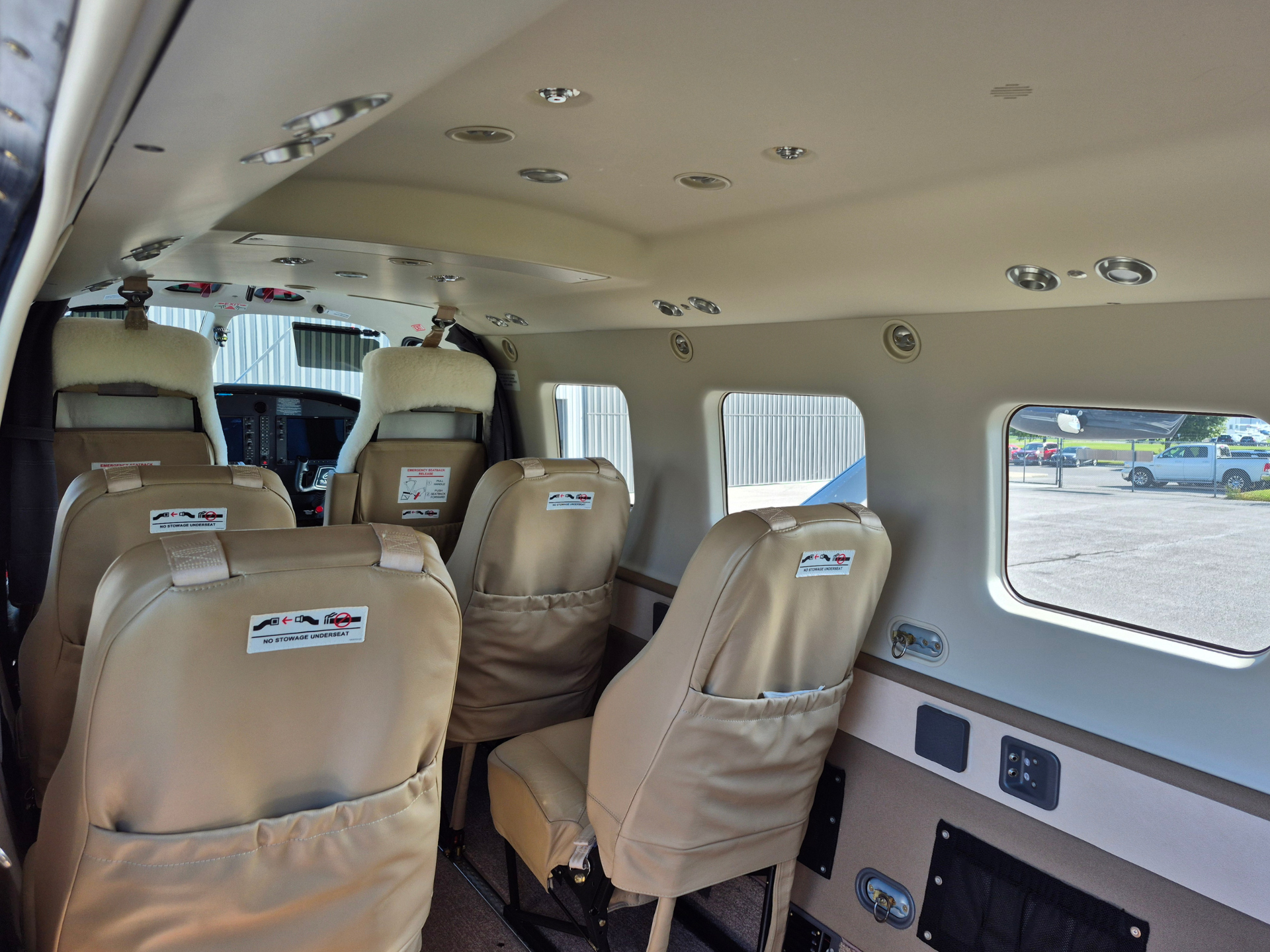 Interior of small passenger aircraft cabin with beige seats and overhead panels view toward cockpit and windows showing tarmac outside