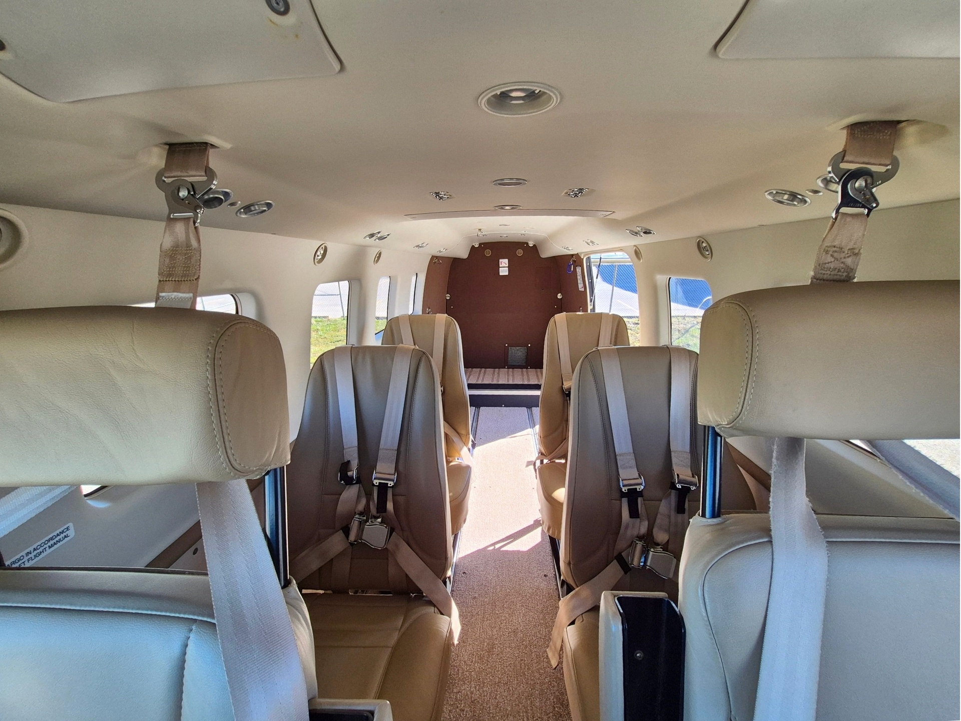 Interior of a small passenger plane with beige seats and seat belts along an aisle toward the back wall