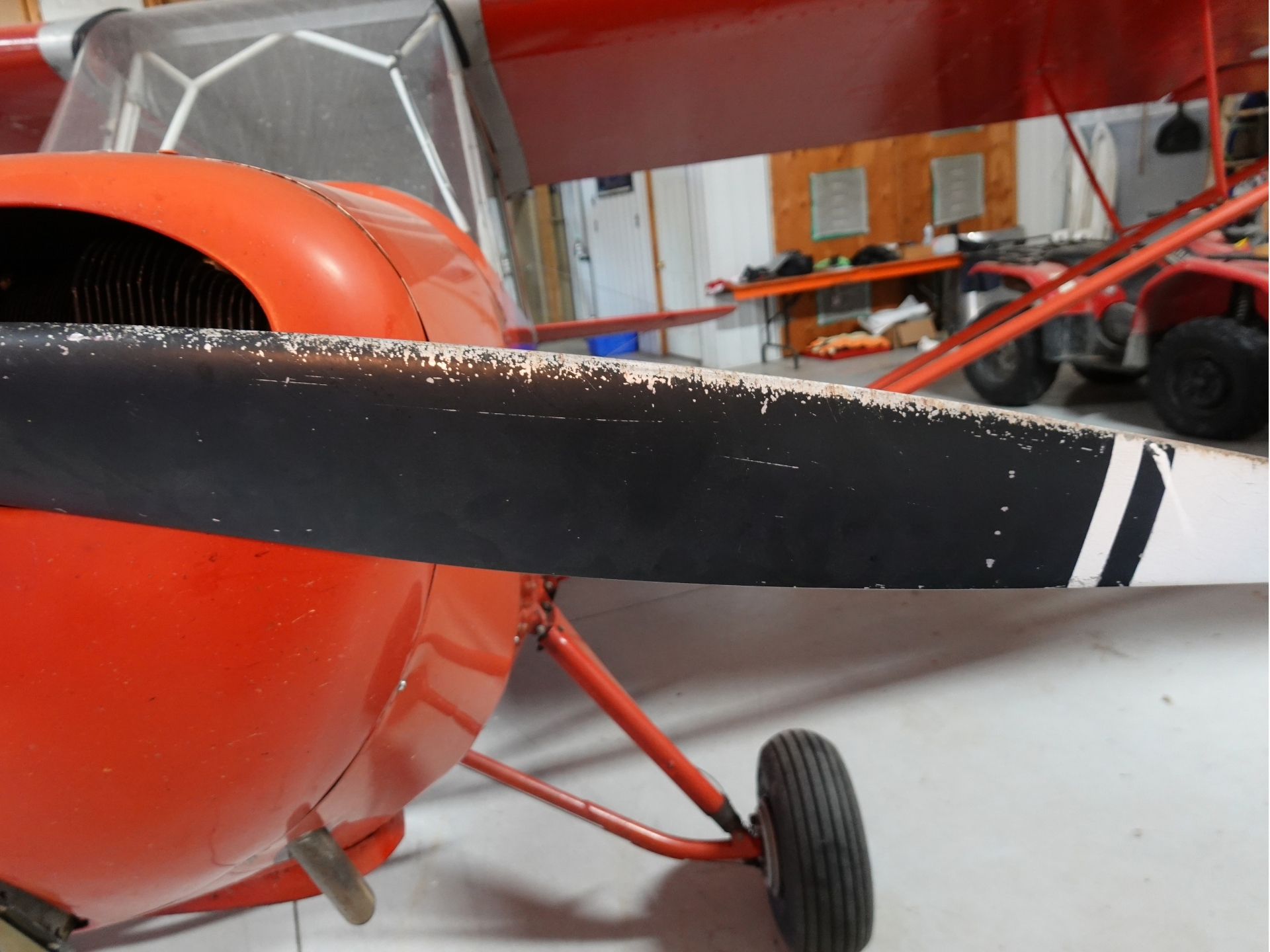 Close up of a red vintage airplane fuselage with a black stripe and landing gear in a workshop