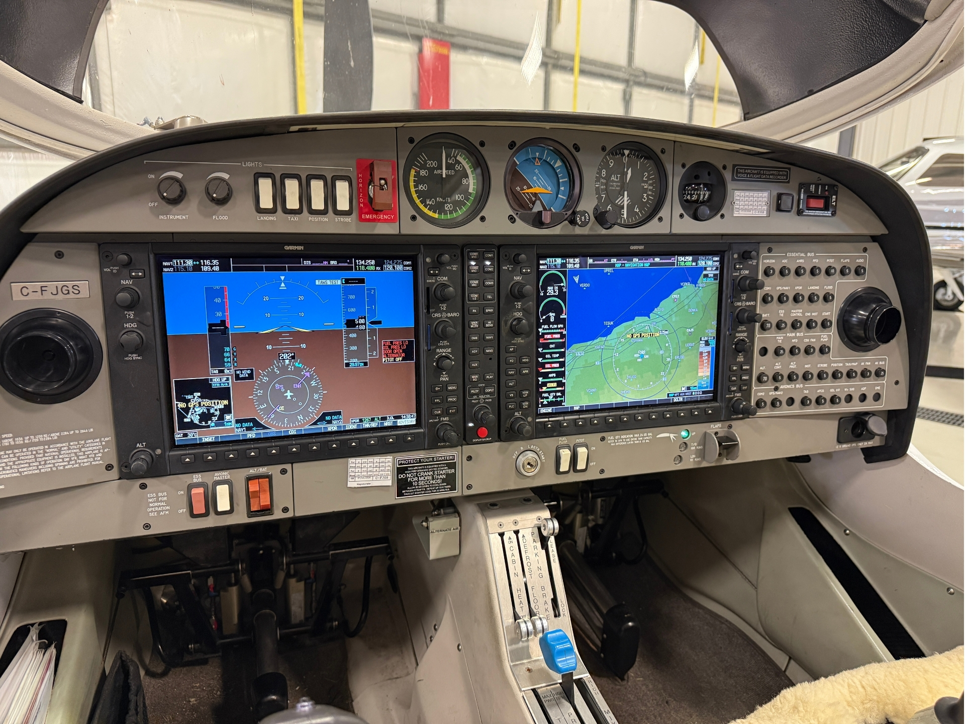 Cockpit of a small airplane with two Garmin glass flight displays, analog gauges, and throttle levers on a gray instrument panel.